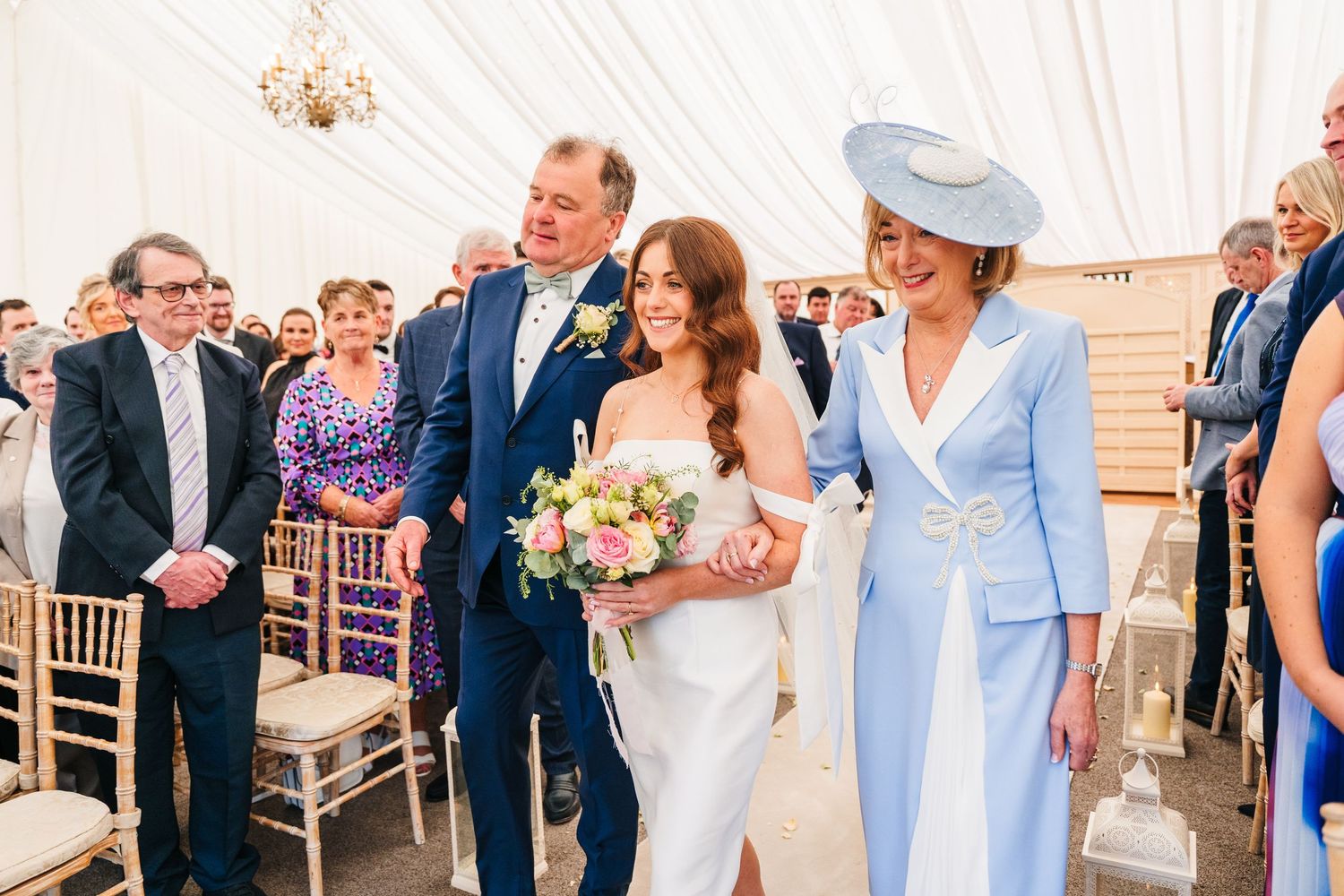 Castle Leslie Wedding Photographer Elegant wedding ceremony in white draped tent with bride holding bouquet beside guests in formal attire.
