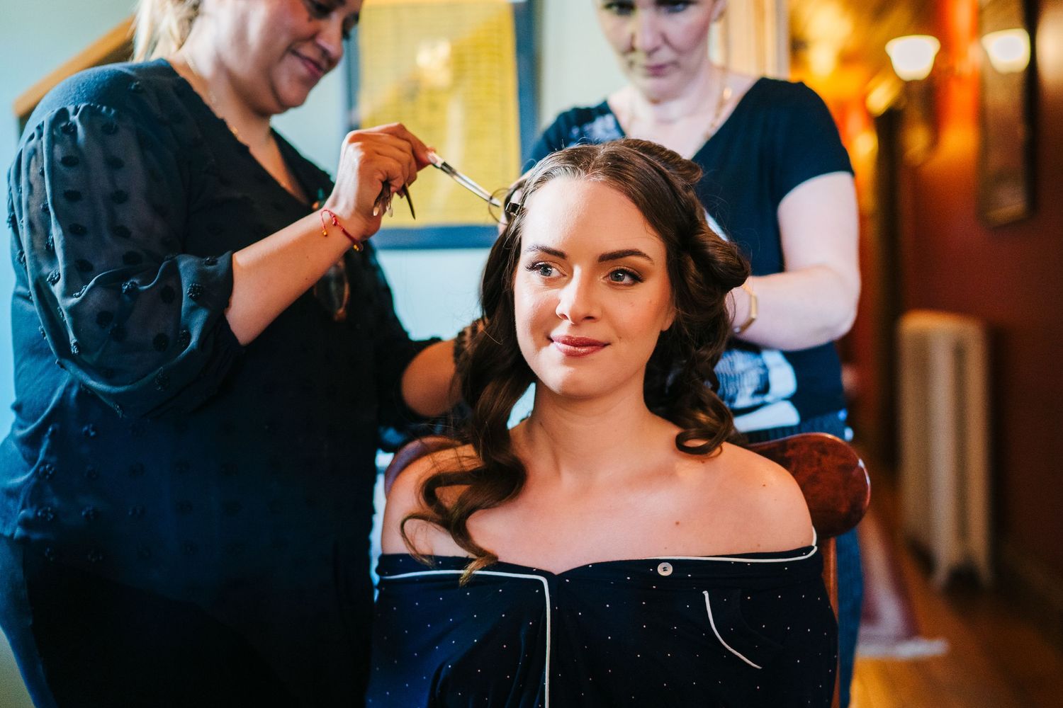 Poulaphouca Wedding photographer wicklow  Wedding preparations with stylists working on bridal hair and makeup in a warmly lit room.