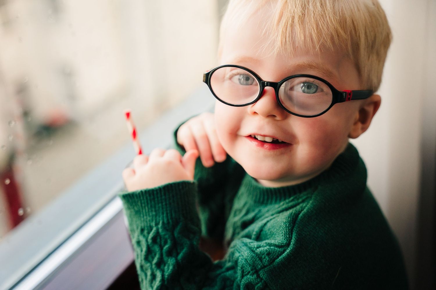 A cheerful child in glasses and a green sweater looks upward with a bright smile. Wedding PHOTOGRAPHER Trim Castle