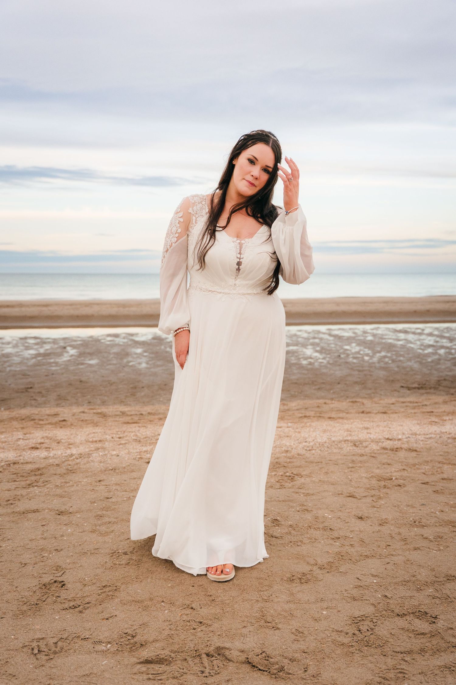 Bride in flowing white dress poses on beach at sunset with natural light. Portmarnock Hotel Wedding PHOTOGRAPHER Dublin