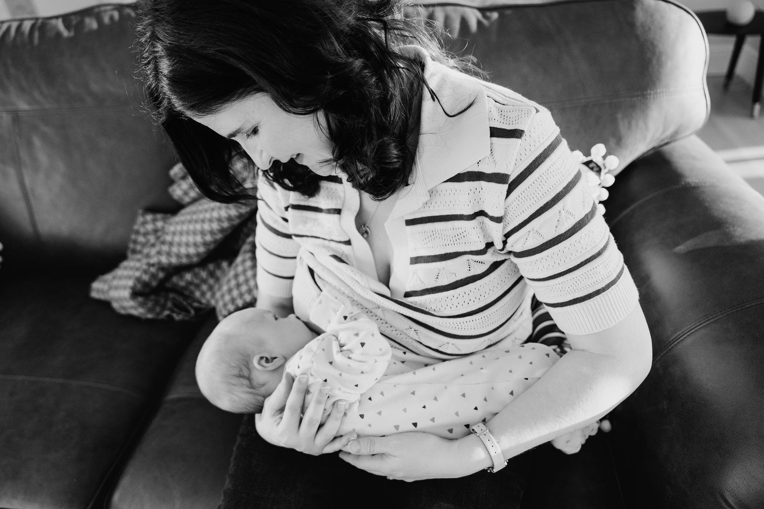 Black and white photo showing a breastfeeding moment on a couch with a striped sweater. Family PHOTOGRAPHER Dublin