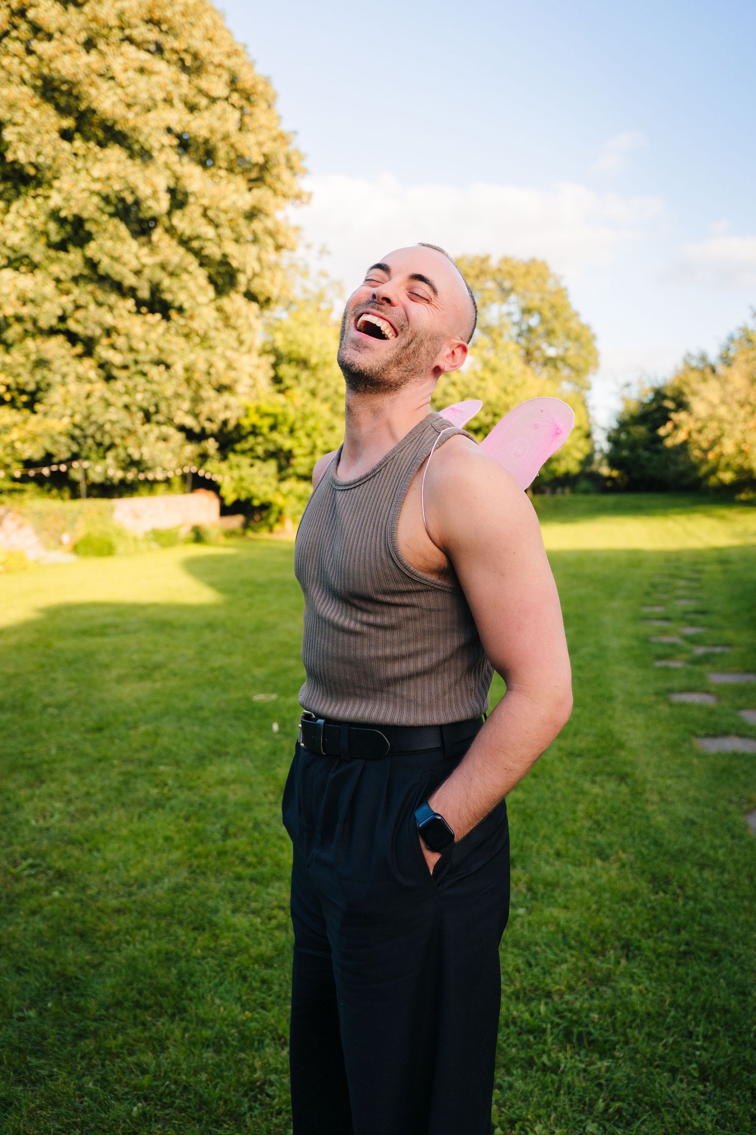 Someone in a sleeveless top and dark pants stands outdoors expressing joy and laughter in a sunny field. . Village Barn Tyrrellspass wedding
