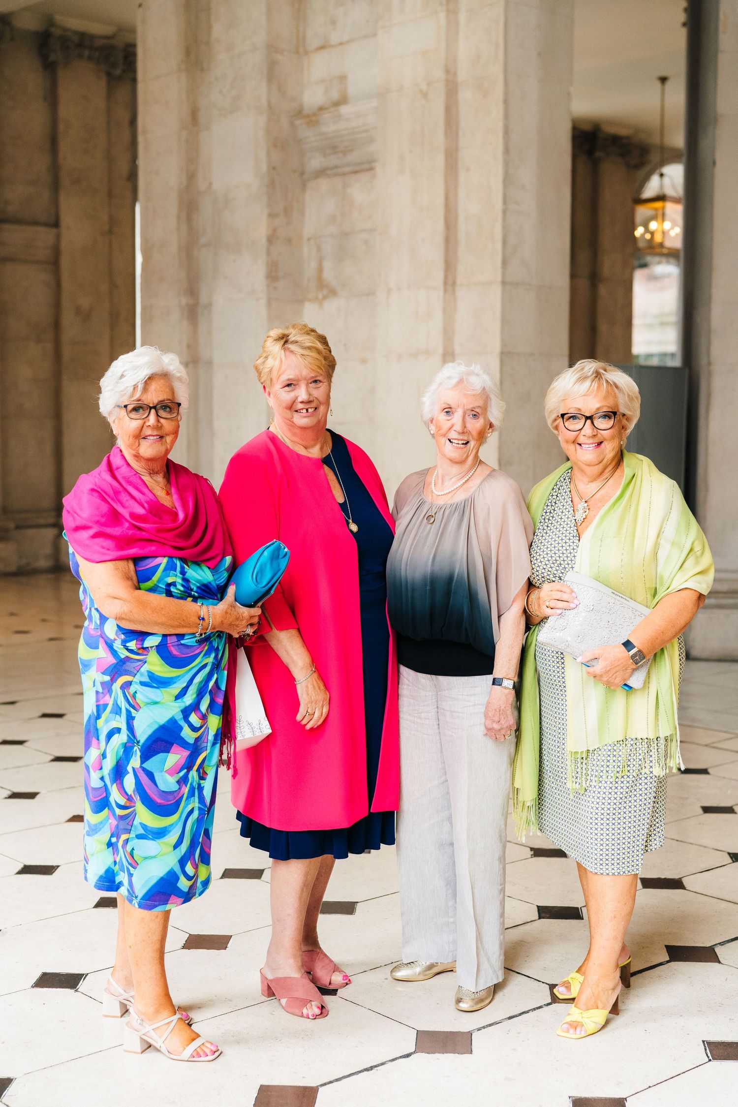 Four women in colorful summer dresses stand together on a checkered floor in an elegant indoor setting.  city hall dublin wedding photos