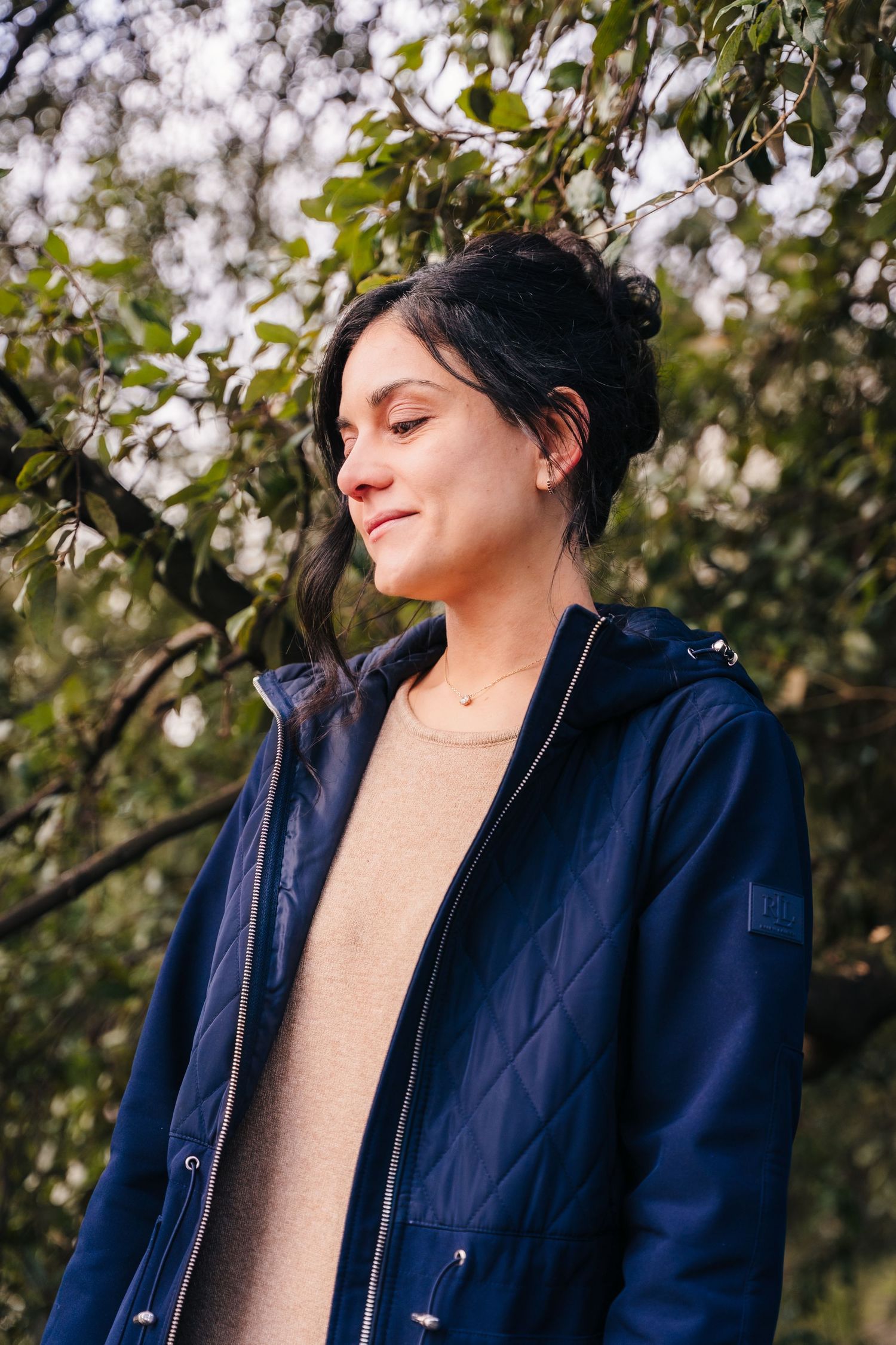 A person wearing a navy quilted jacket and beige sweater poses against a natural outdoor background. professional headshots dublin