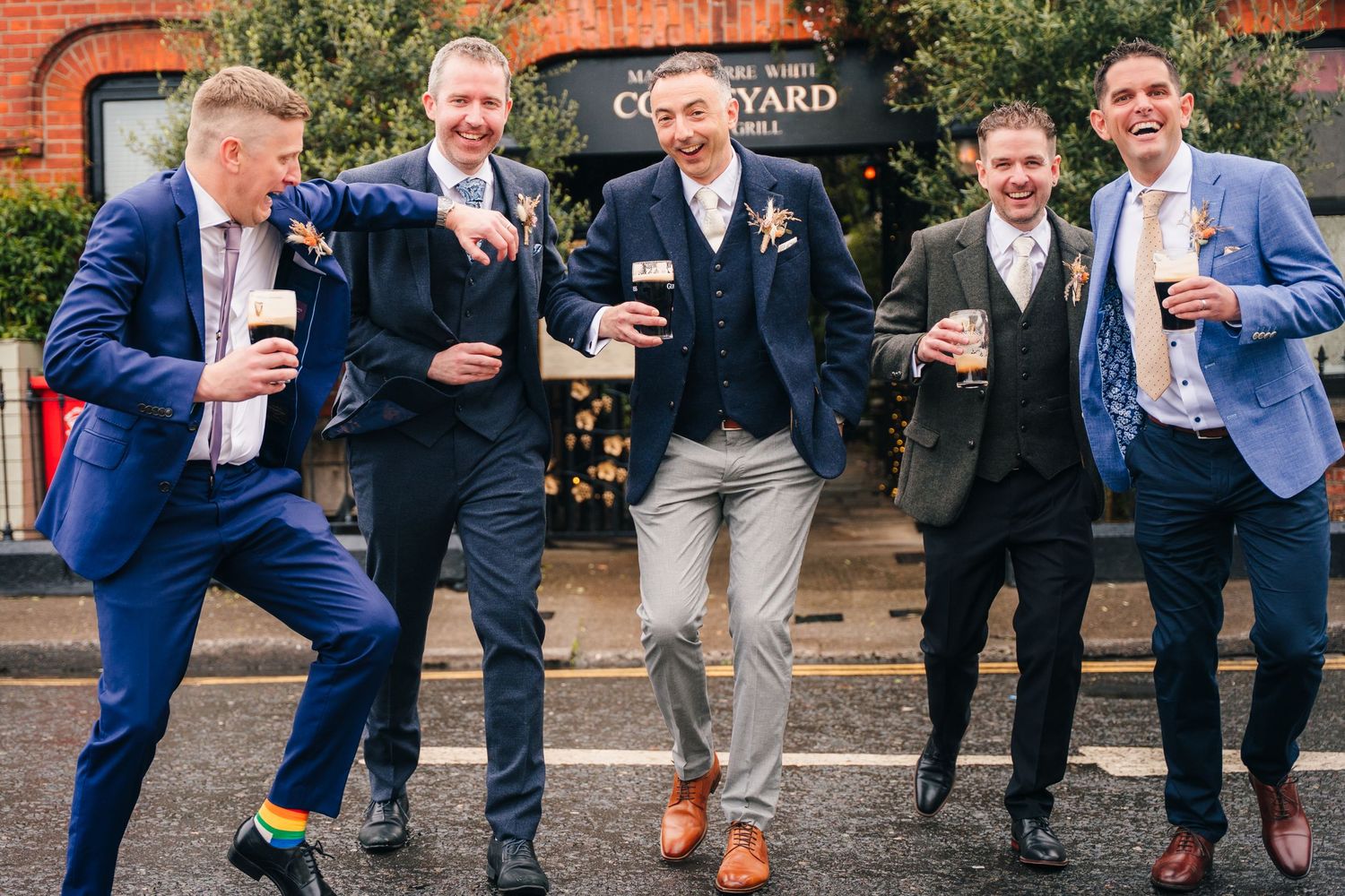 Group of men in suits posing outside a brick building with drinks. Marco Pierre Dublin Wedding Photographer