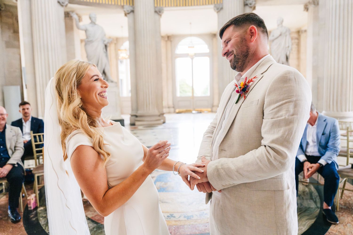 A happy couple exchanges rings during their wedding ceremony in an elegant room with white columns. Wedding PHOTOGRAPHER Dublin