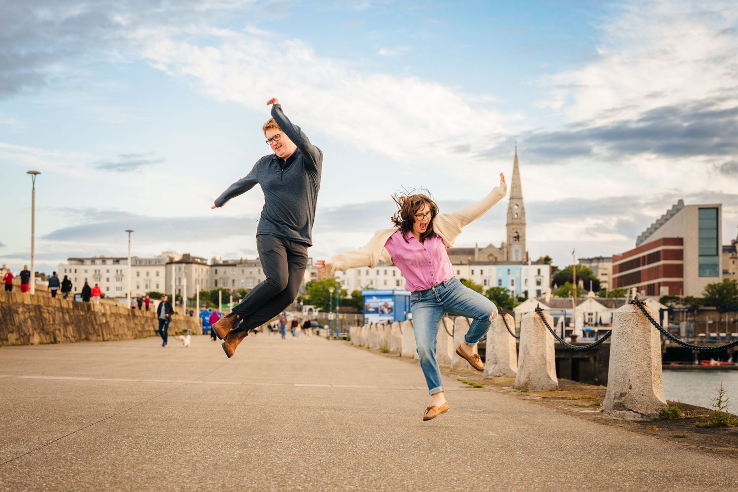 Two energetic friends leap joyfully in the air at sunset near a waterfront promenade. PHOTOGRAPHER Dublin ireland