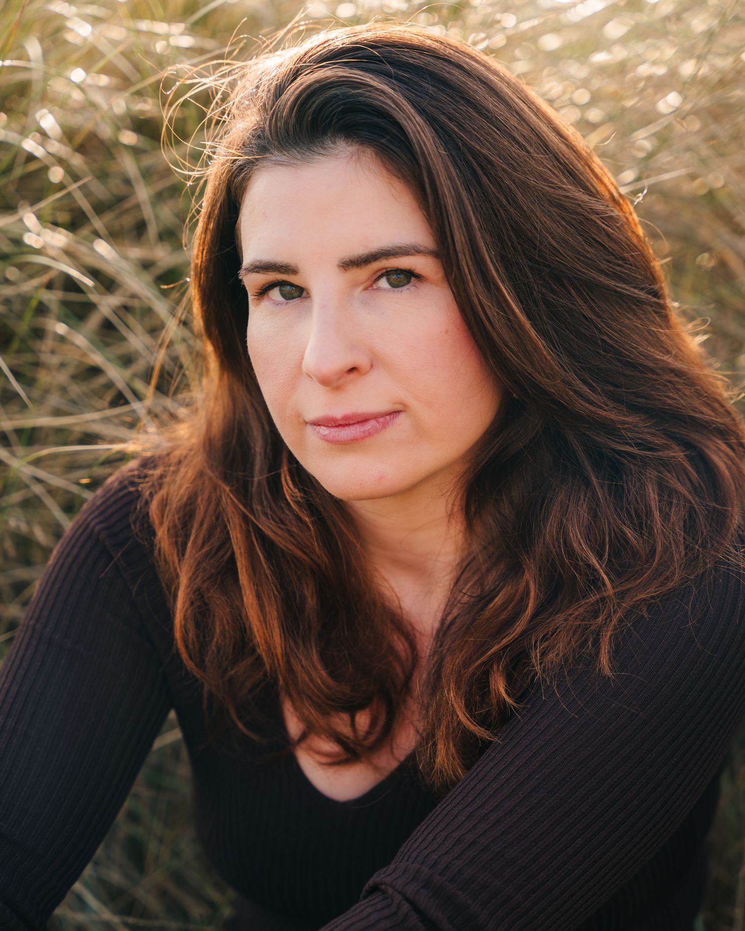 Close up outdoor portrait with flowing dark hair and black sweater against sunlit wheat field background. PHOTOGRAPHER Dublin ireland