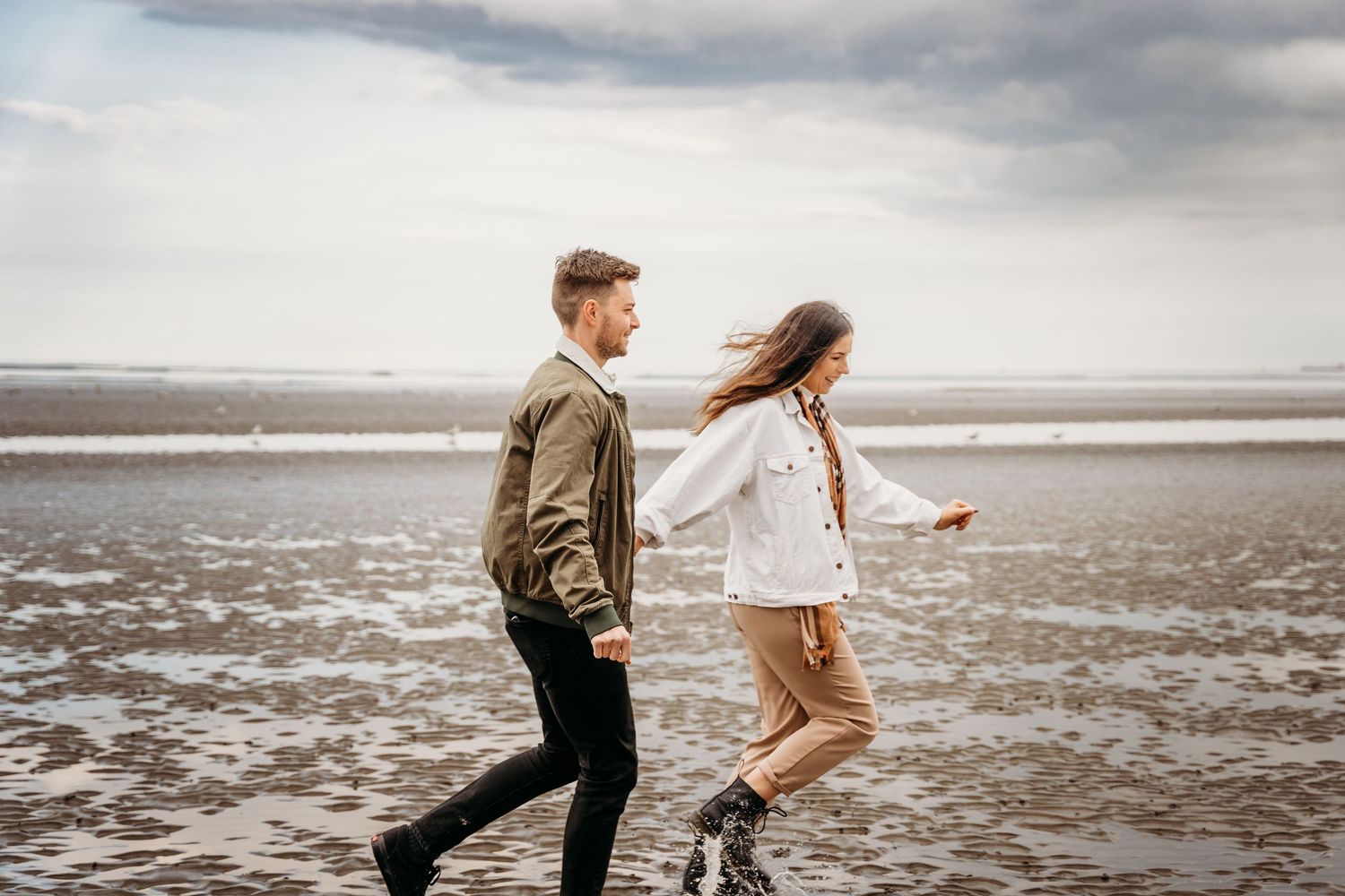 A couple runs and plays together on a misty beach during an overcast day at the seashore. PHOTOGRAPHER Dublin ireland