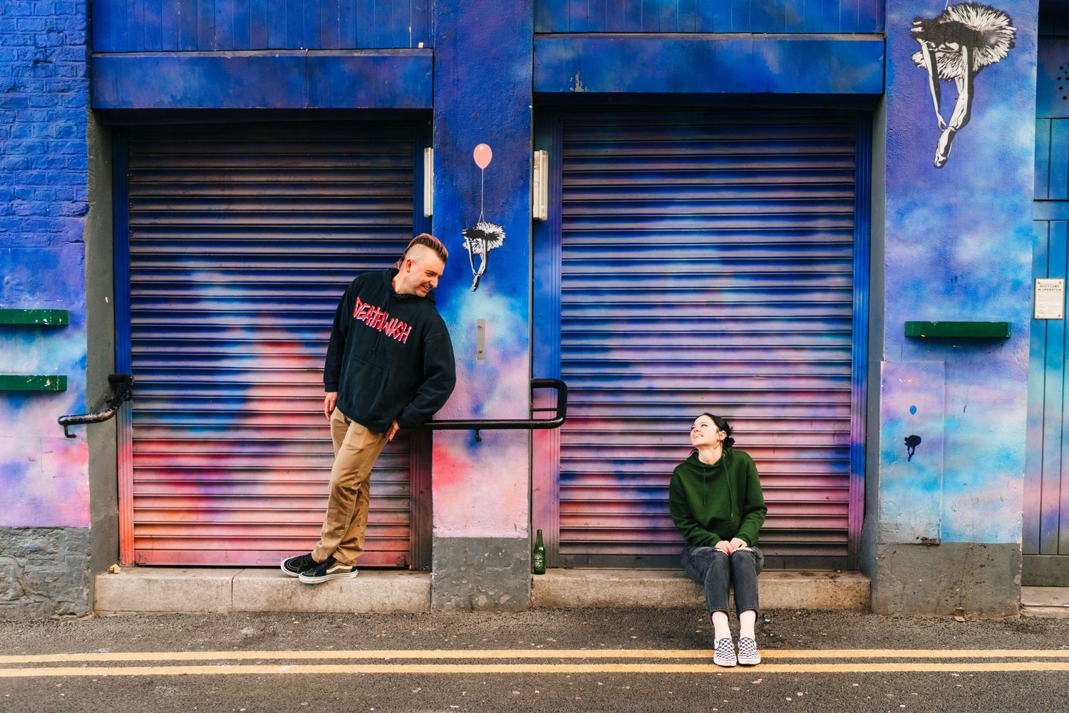 Two people stand against colorful blue metal shutters on an urban street. PHOTOGRAPHER Dublin PHOTOGRAPHER Dublin ireland