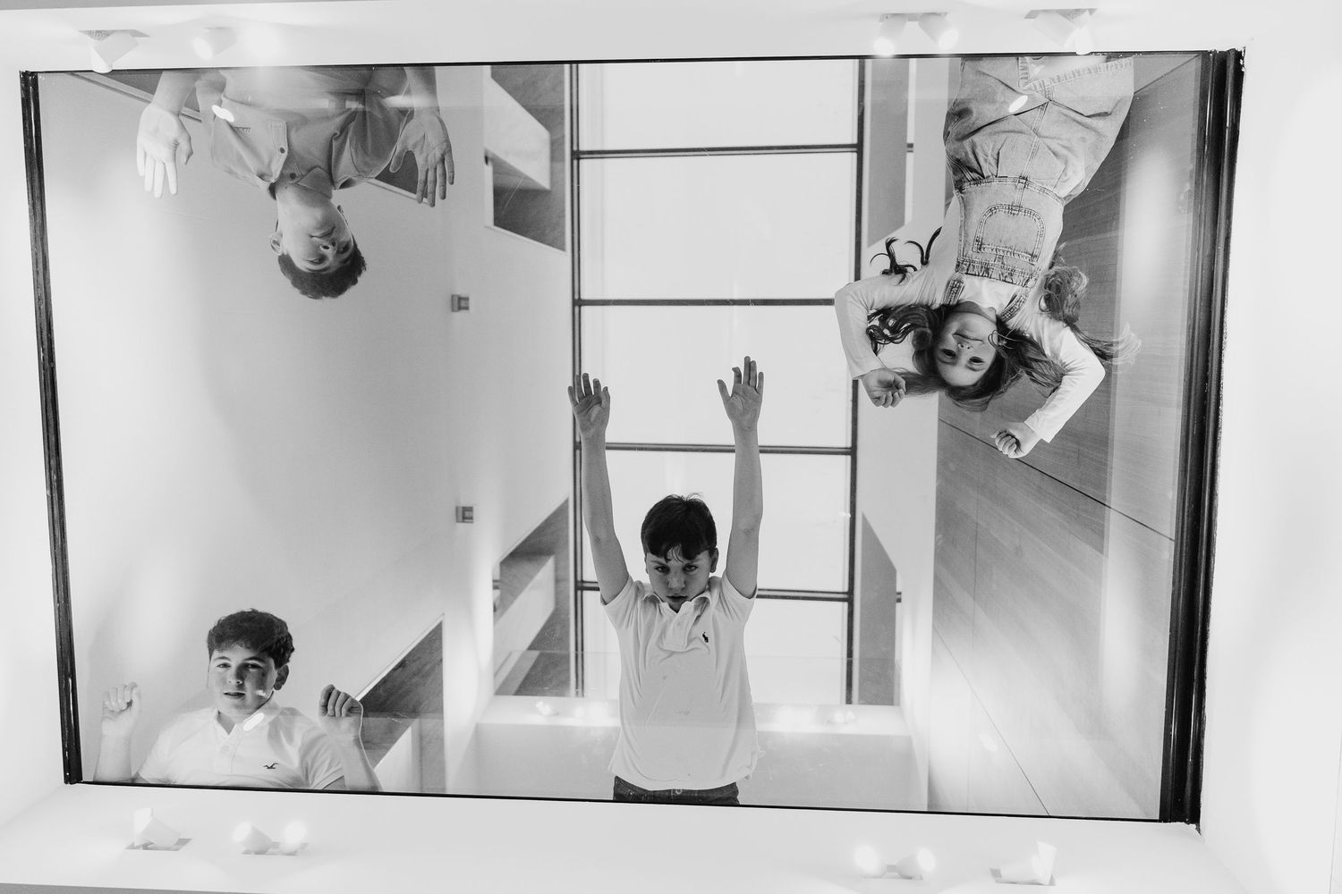 A black and white triptych photograph showing three playful perspectives of a child with arms raised in different poses. family PHOTOGRAPHER