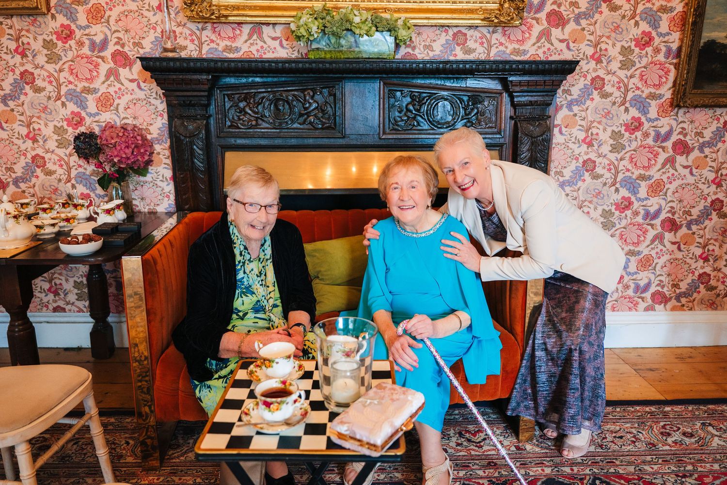 Wedding guests enjoying a meal at tables decorated with floral wallpaper and vintage decor. LGBTQ Ashley Park Wedding Photographer