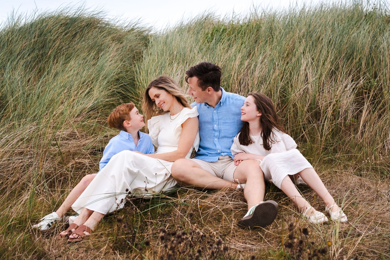 Family lying in coastal dune grass during a casual outdoor photo session.  Family photographer Dublin Ireland
