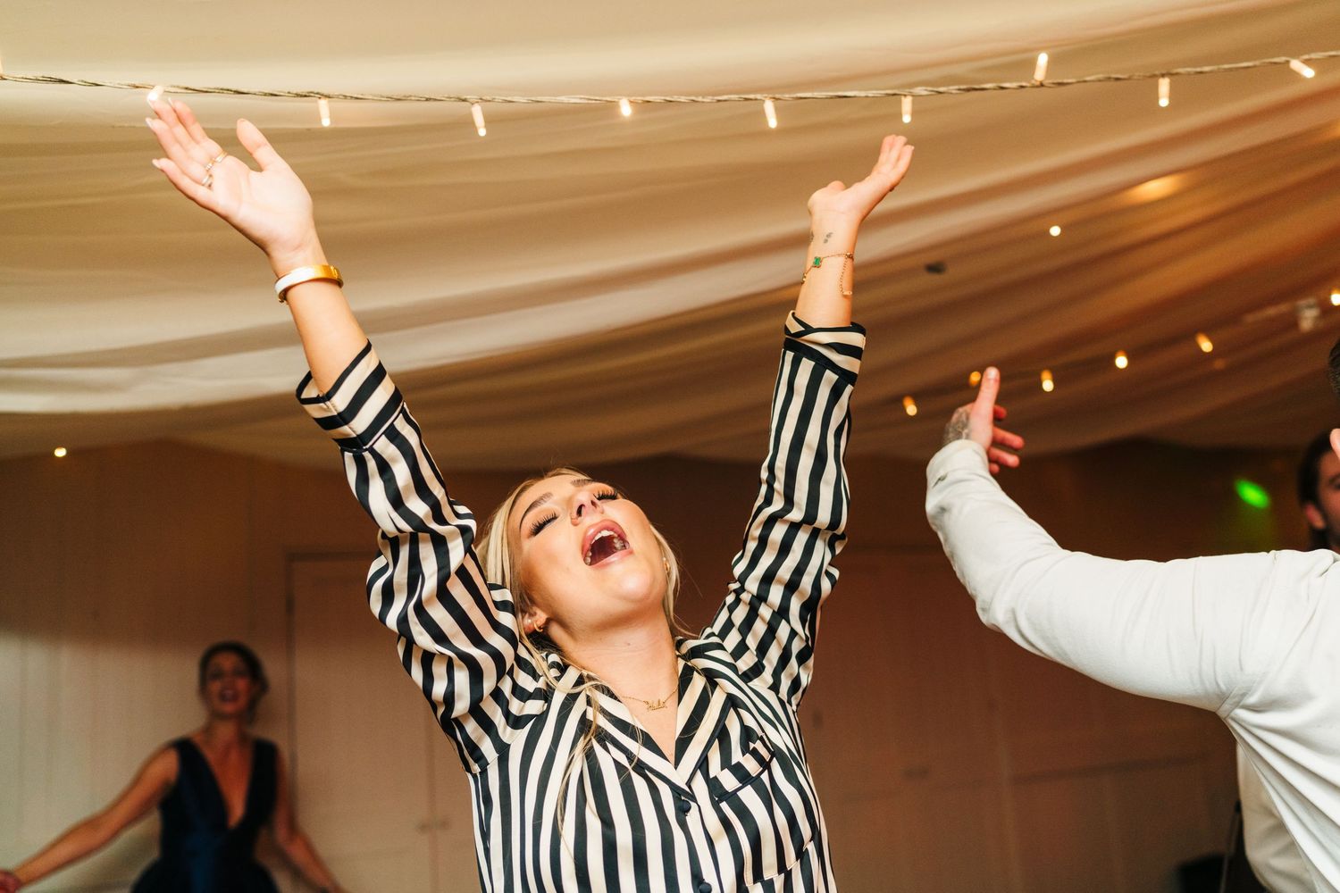 Wedding guests dancing with hands raised under string lights in a decorated tent venue.  Virginia Park Lodge Wedding Photographer Cavan Dubl