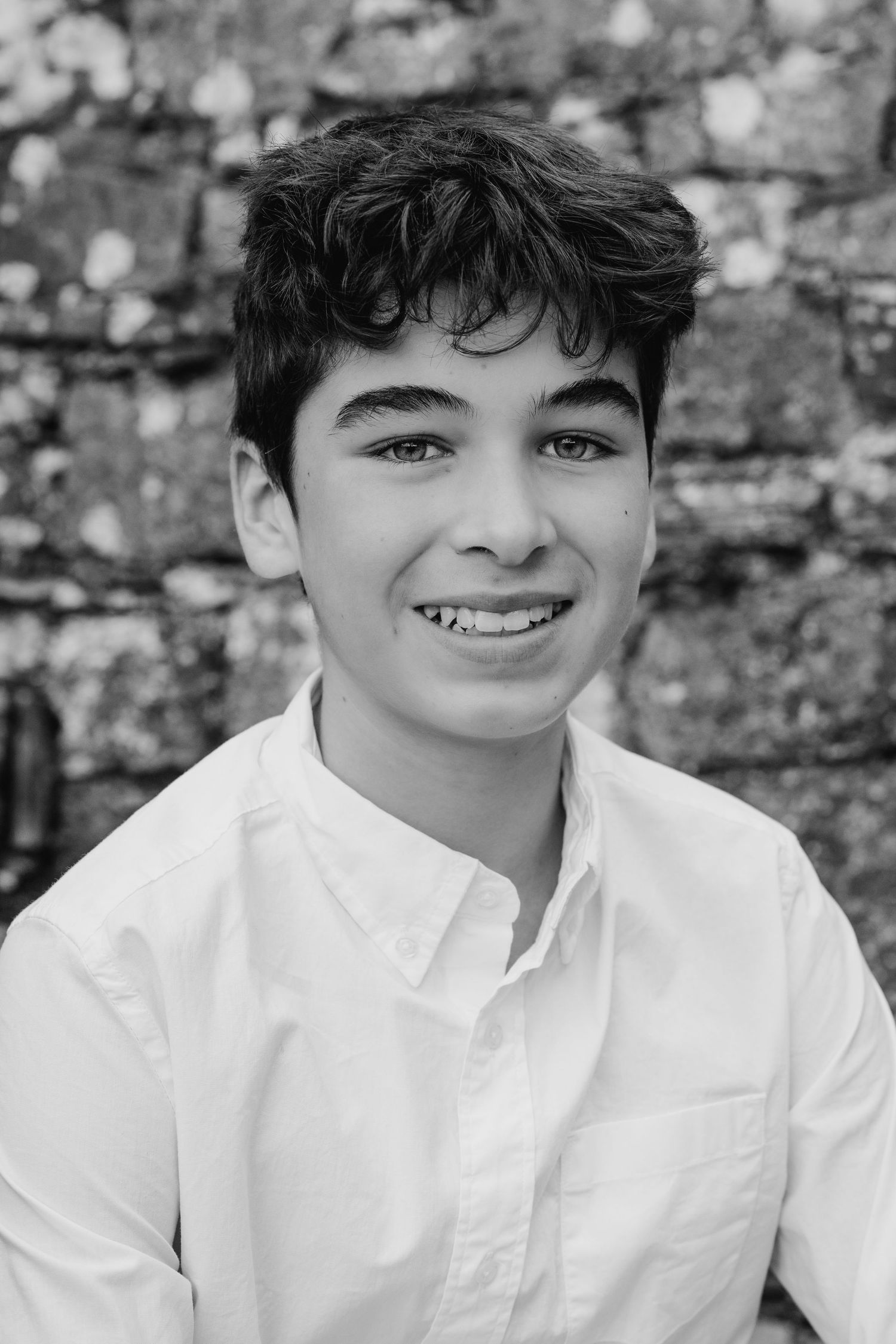 Black and white portrait series showing a young person in a white button-down shirt smiling against a stone wall. BEctive abbey family photo