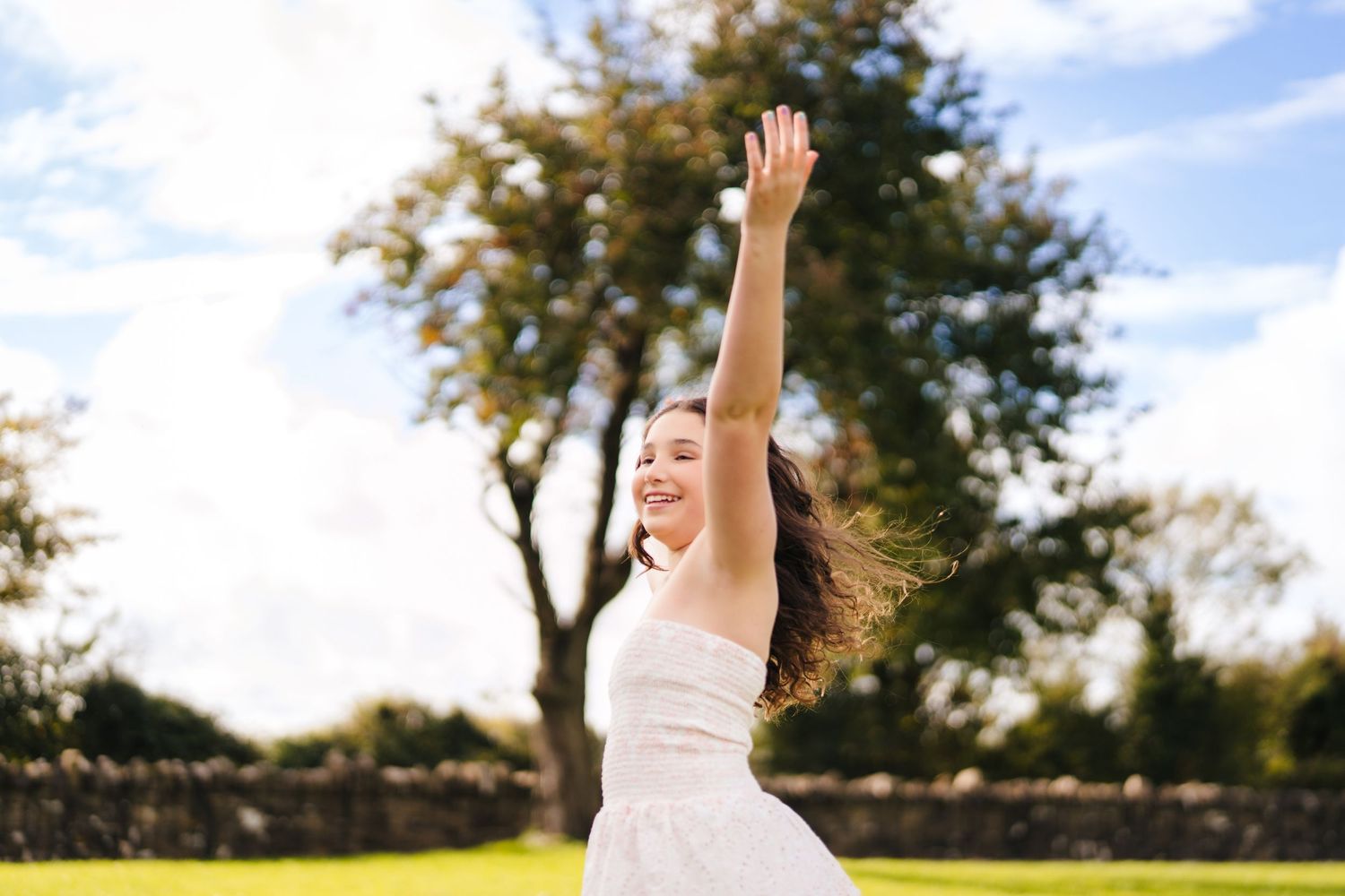 Person in white dress twirling joyfully outdoors with arms raised against blue sky. BEctive abbey family photographer dublin