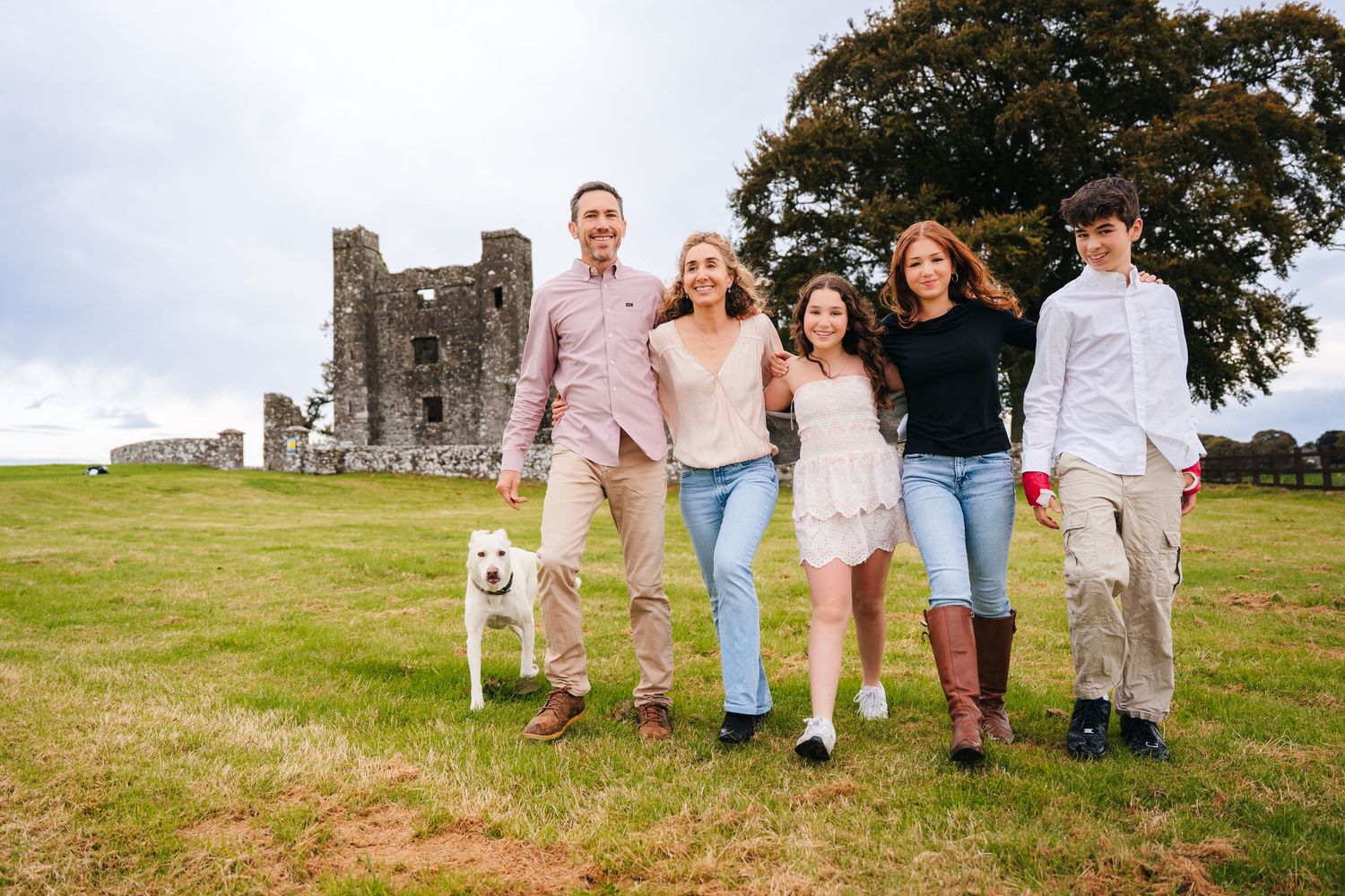 A group walks together along a scenic grassy path near historic stone ruins on a bright sunny day. BEctive abbey family photographer dublin