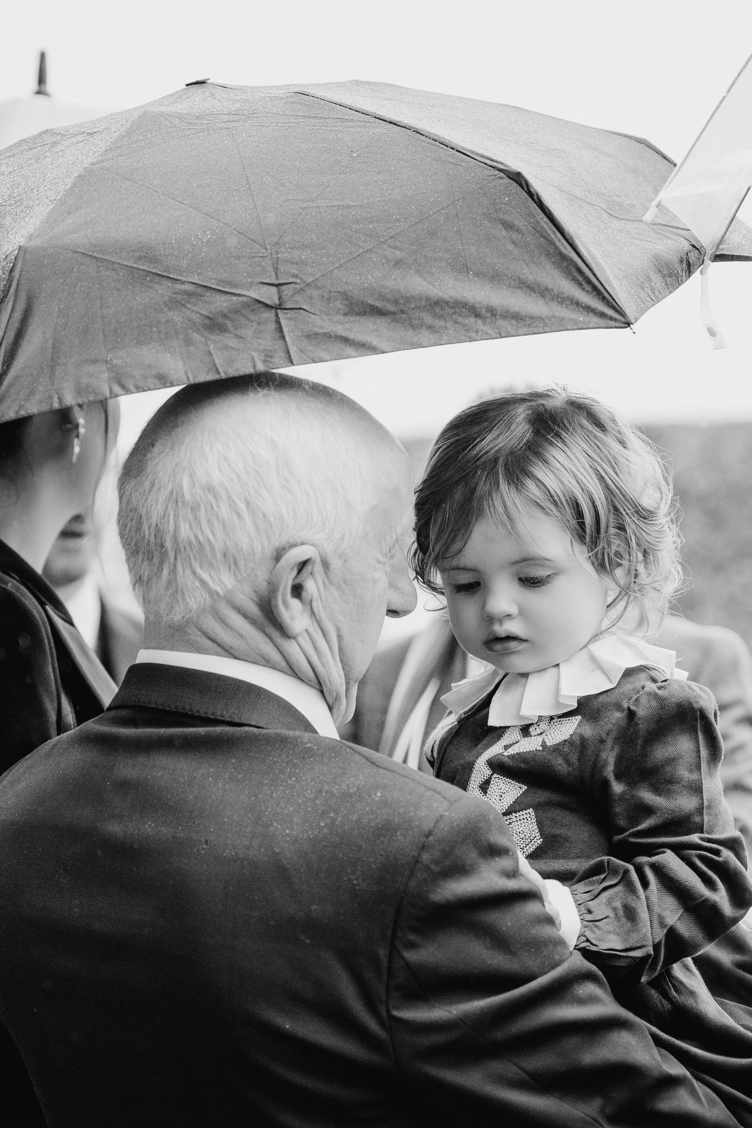 Rainy day wedding moment captured under umbrellas in black and white photography.