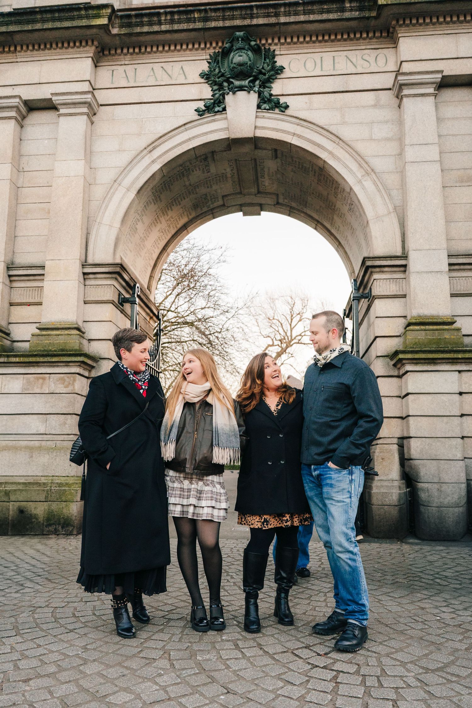 A group of people laughing together under a stone archway on a cobblestone street. family PHOTOGRAPHER Dublin