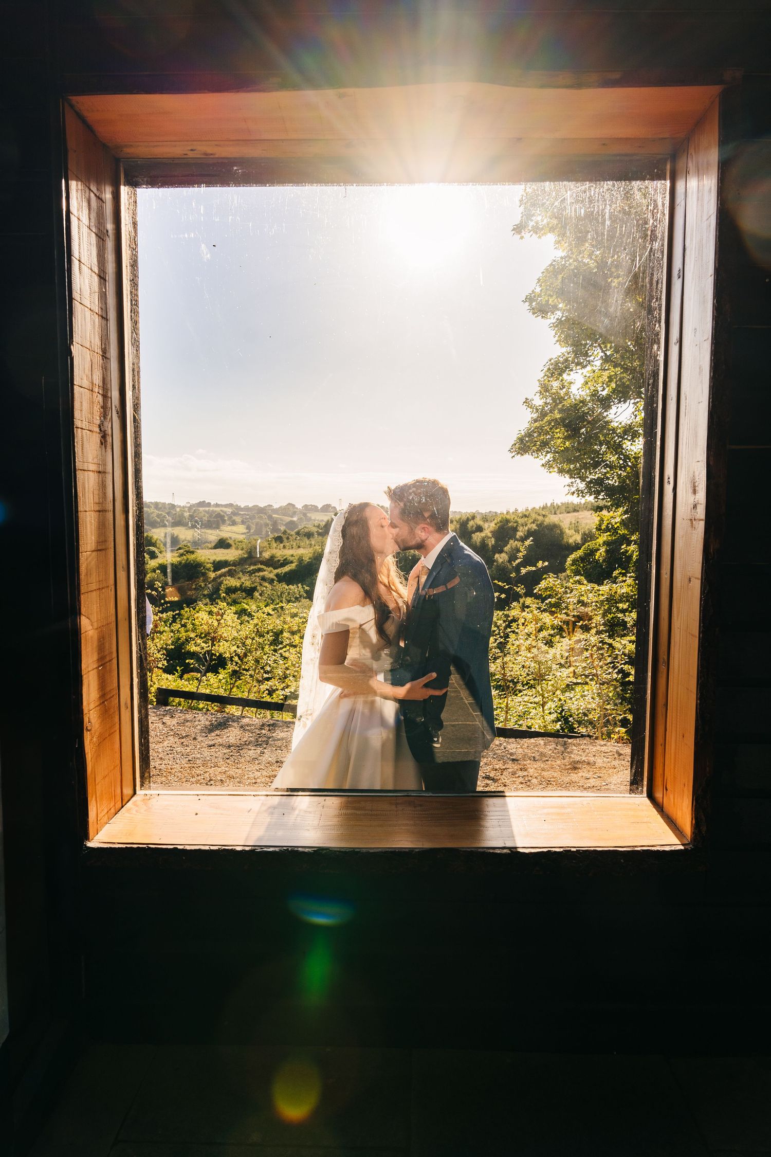 Poulaphouca Wedding photographer wicklow  Romantic silhouette of couple framed in window with scenic countryside view in background.