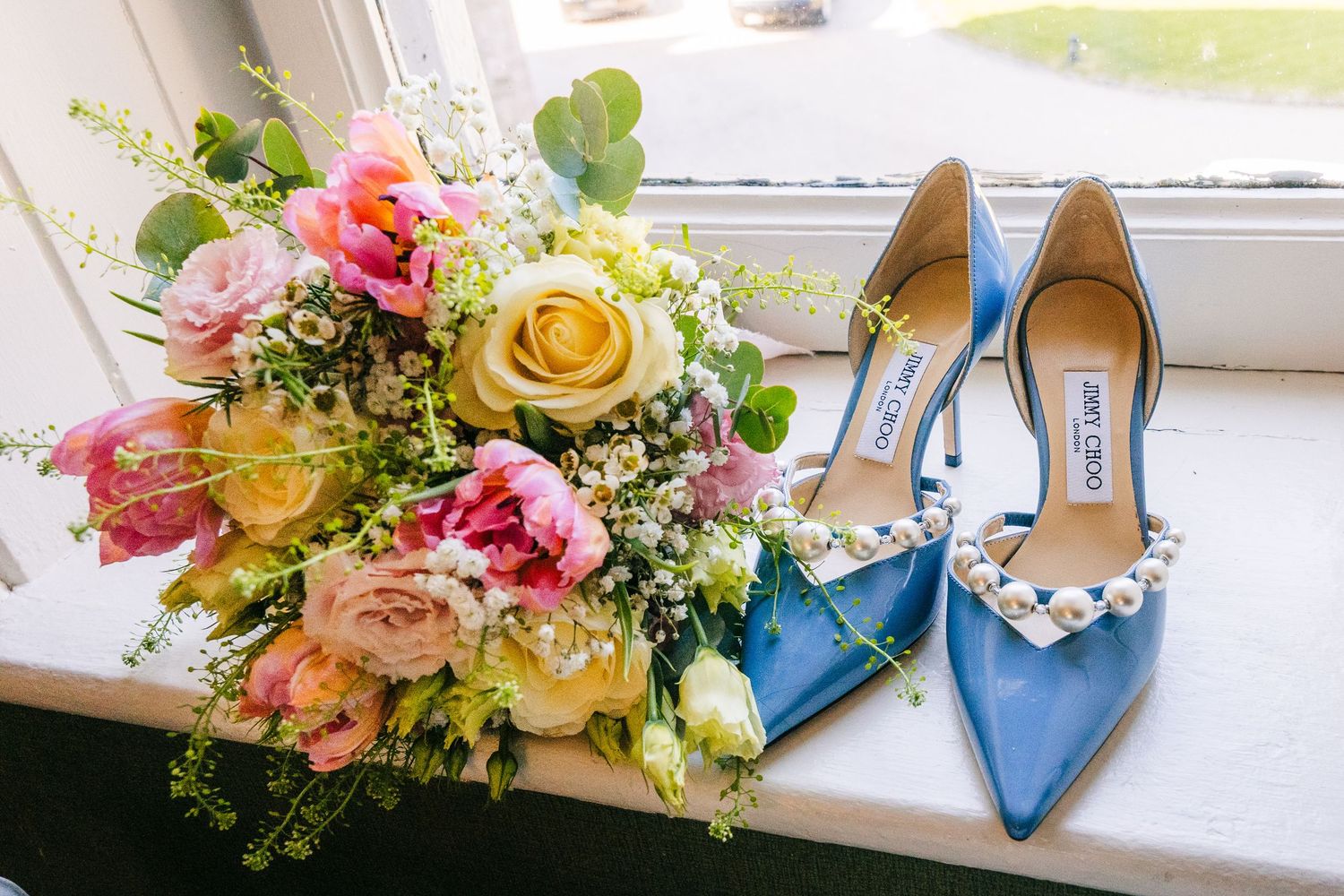 Castle Leslie Wedding Photographer DubElegant blue wedding shoes next to a vibrant bouquet of pink, yellow and coral roses on a windowsill.