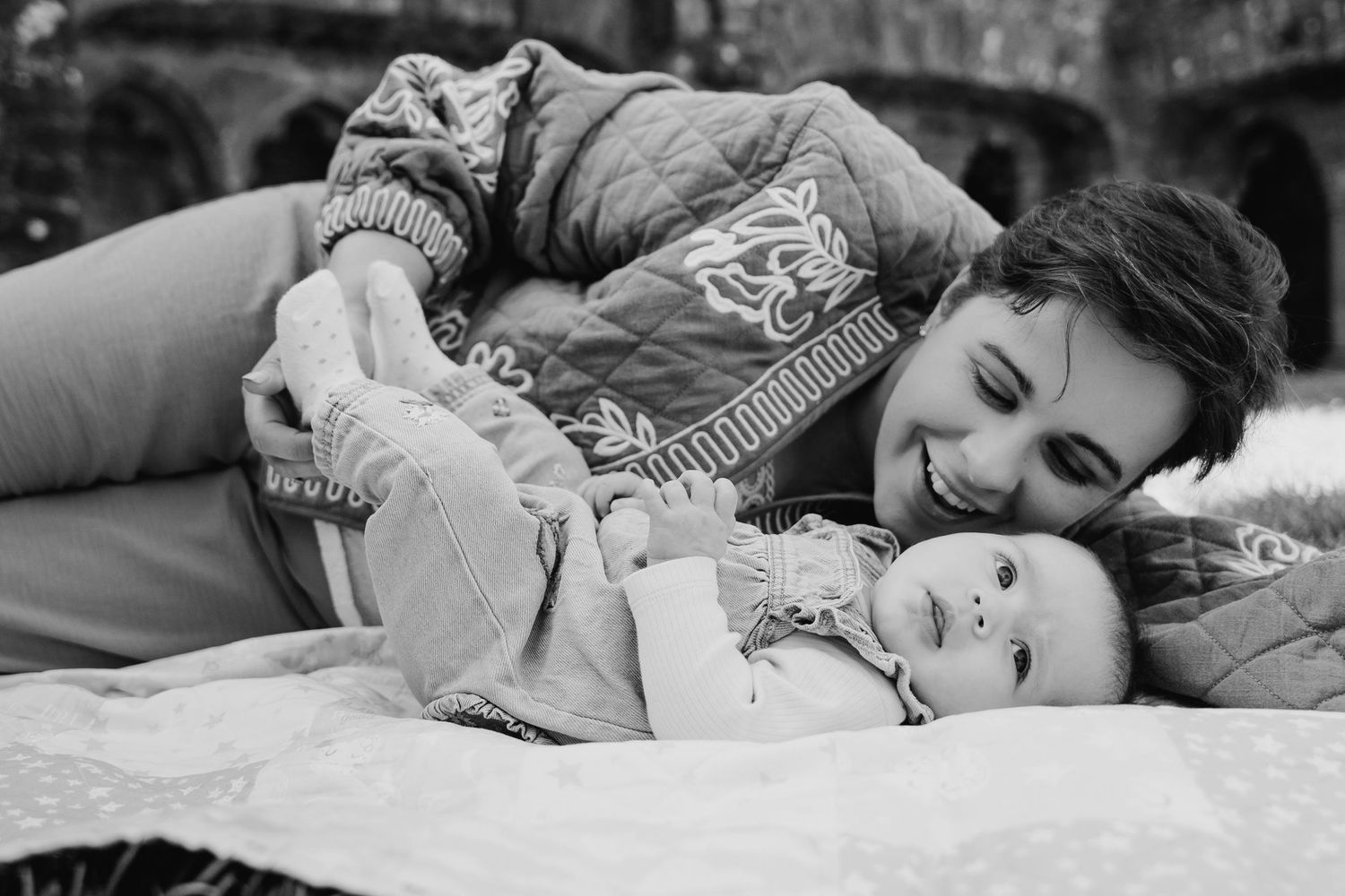Black and white portrait of a parent and child lying together on a blanket in an intimate embrace.Family PHOTOGRAPHER Dublin