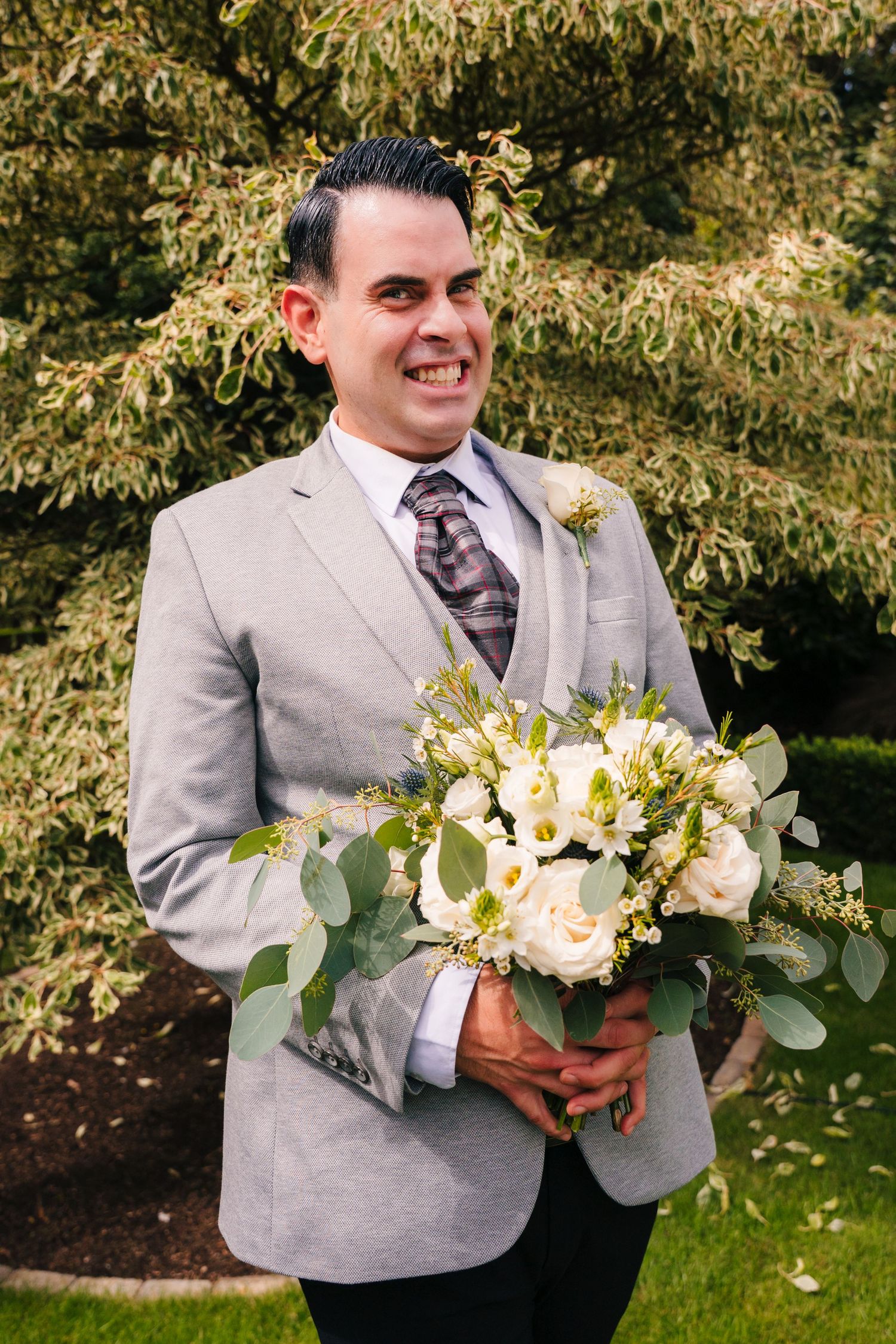 Groom in light grey suit holding elegant white and green floral wedding bouquet outdoors. Portmarnock Hotel Wedding PHOTOGRAPHER Dublin