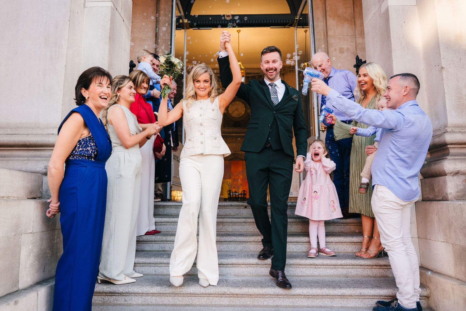 Wedding party celebrating on grand stone steps with joyful dance moves. City Hall Dublin wedding photogrAPher