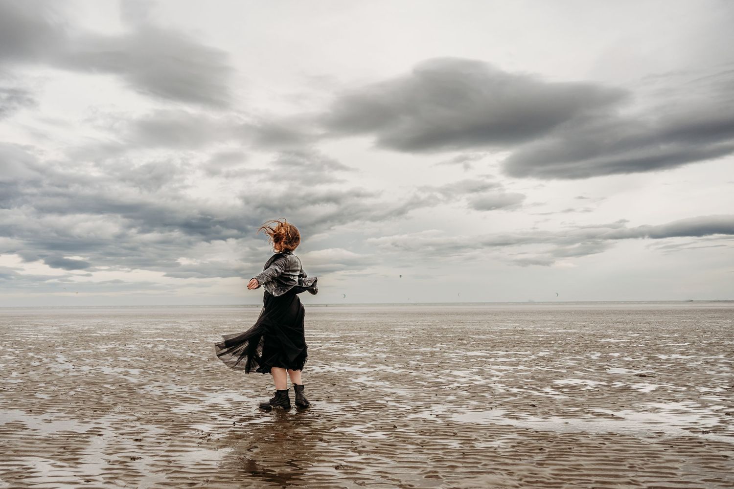 Two people embrace on a misty beach shoreline with dramatic cloudy skies overhead. engagement PHOTOGRAPHER Dublin