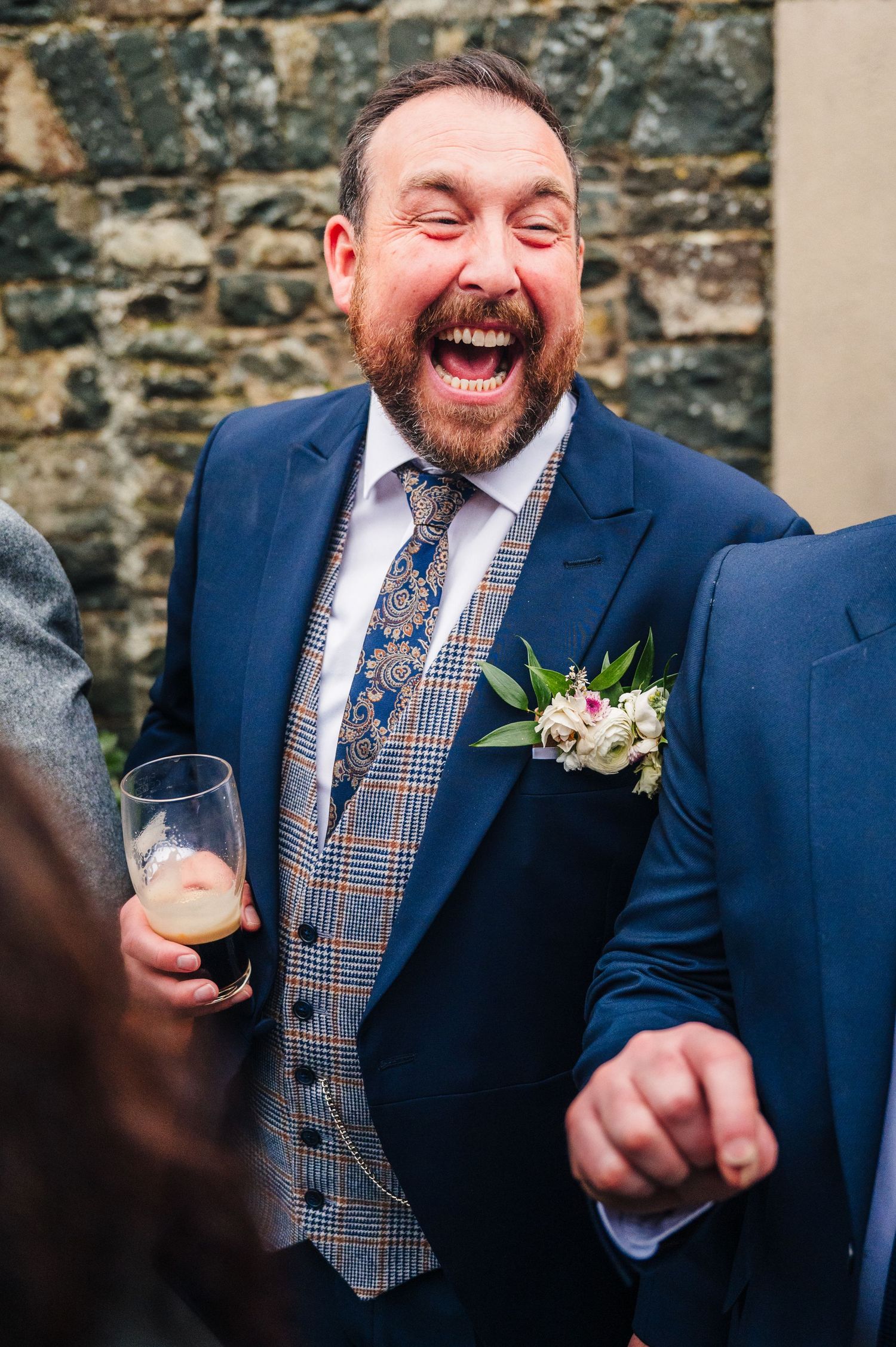 A person in a navy suit and plaid tie laughs heartily during a wedding celebration.  Virginia Park Lodge Wedding Photographer Cavan Dublin I