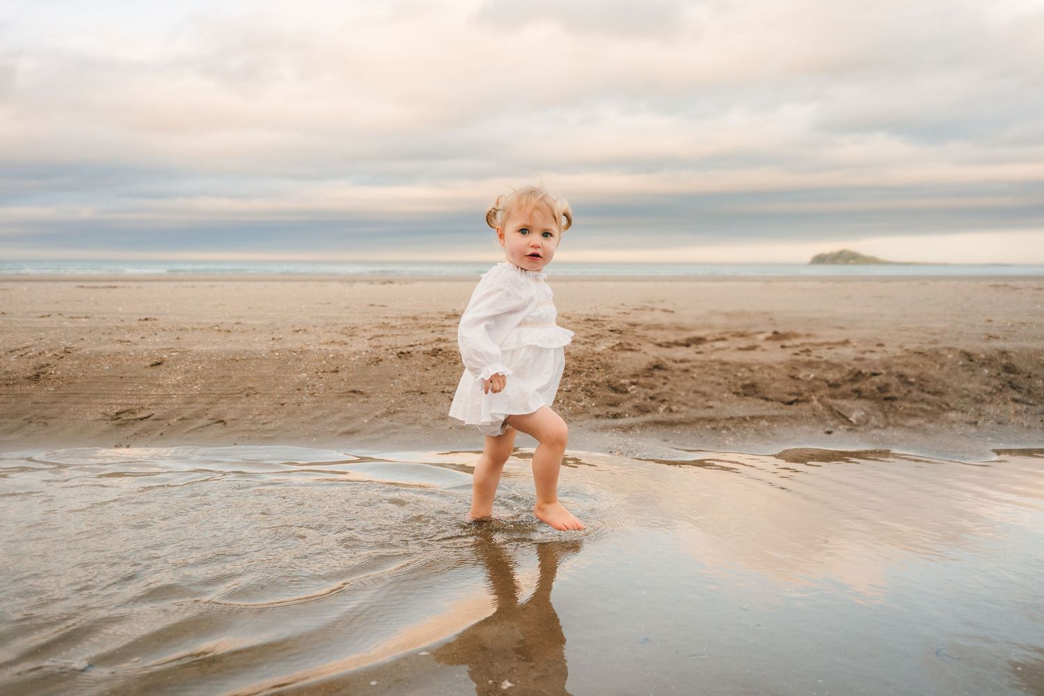 Young child in white running through shallow ocean water at sunset.