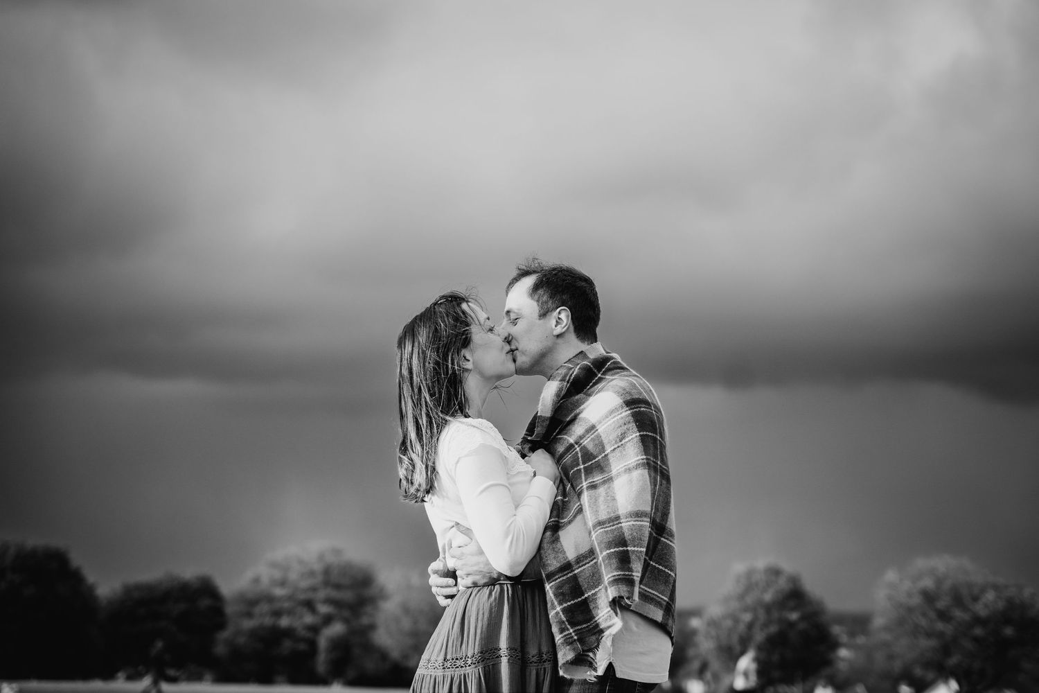 A romantic couple embraces and kisses outdoors in black and white, with one wearing a plaid flannel shirt. PHOTOGRAPHER Dublin ireland