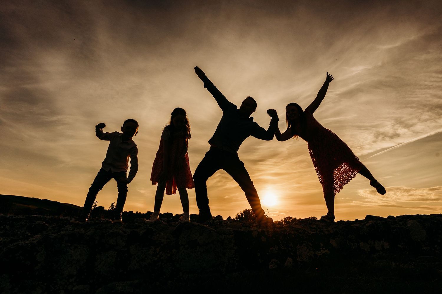 Silhouettes of people jumping and posing against a dramatic sunset sky creating a fun group photo composition. family PHOTOGRAPHER Dublin