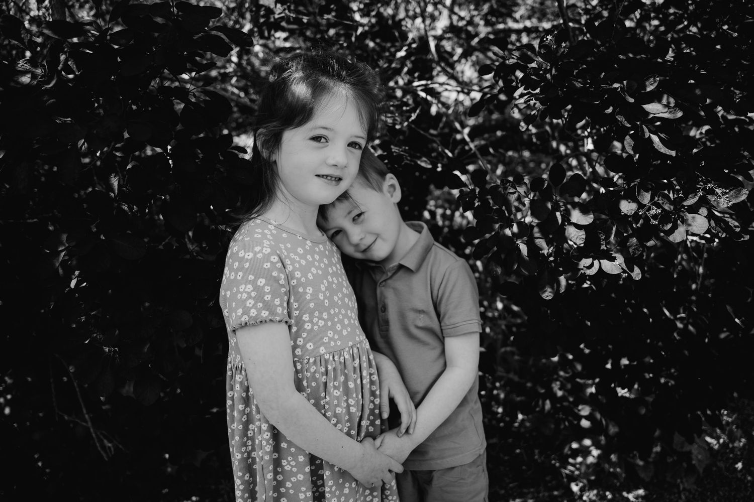 A couple in vintage clothing embraces in a romantic black and white portrait scene among trees and foliage. family PHOTOGRAPHER Dublin