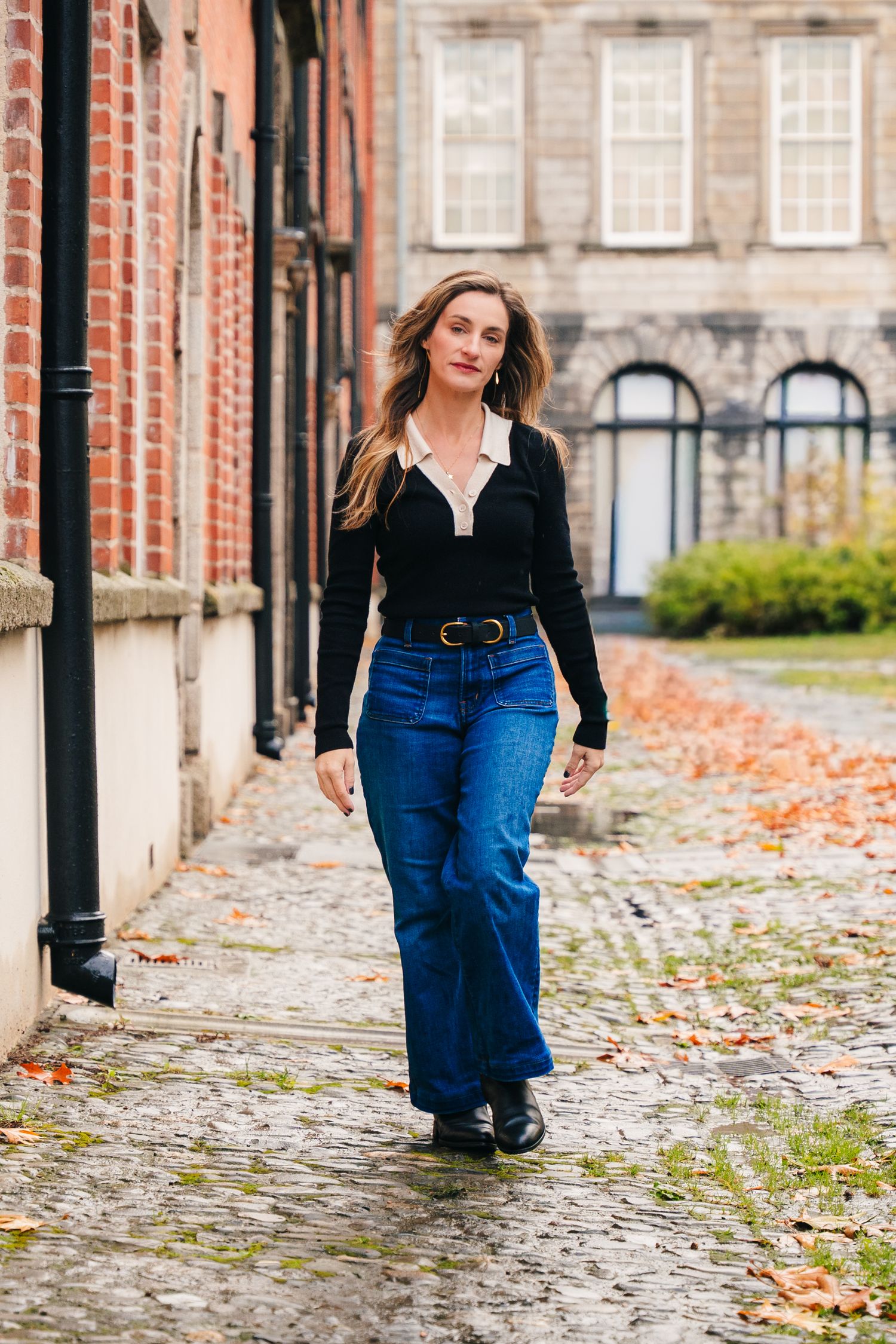 Person walking on cobblestone path wearing blue jeans and black jacket near brick building. professional headshots dublin photographer