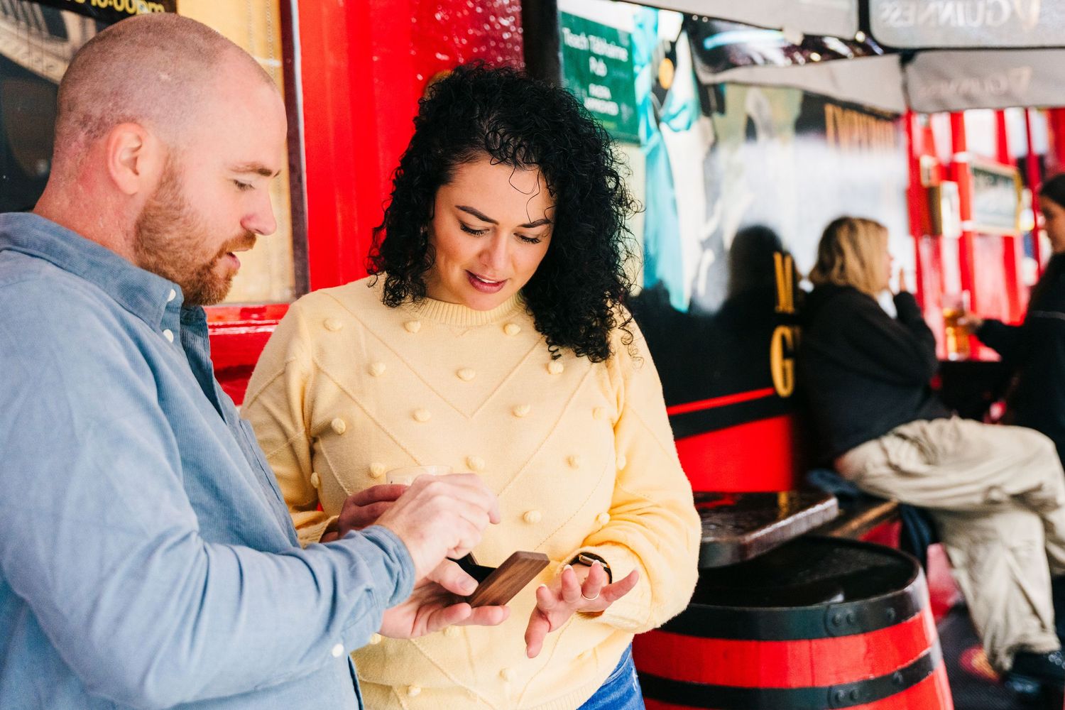 Two people looking at something together on a mobile device in front of a red wall and cafe counter. Proposal Dublin Photographer