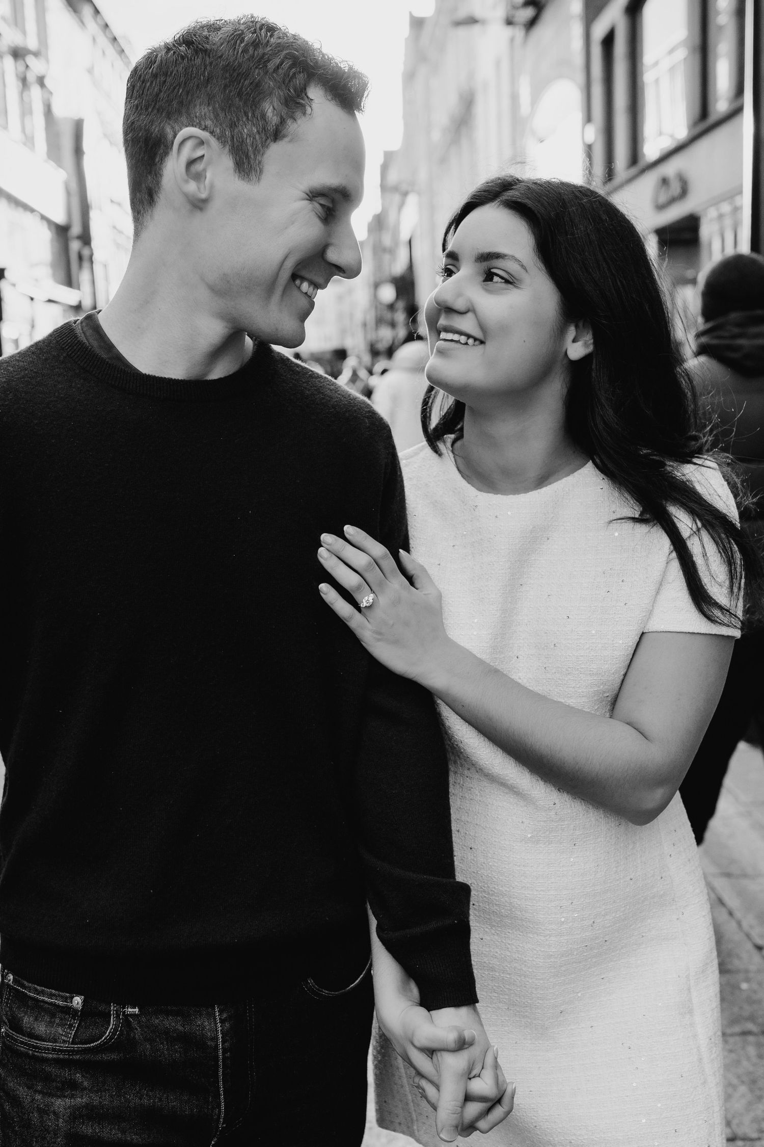 Romantic black and white portrait of a happy couple gazing at each other while holding hands on a city street. Surprise proposal dublin phot