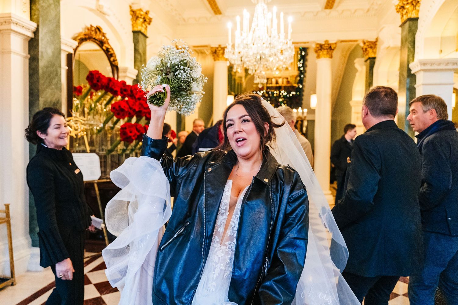 A candid moment at a wedding reception with guests celebrating in an ornate venue with chandeliers. Wedding PHOTOGRAPHER Dublin