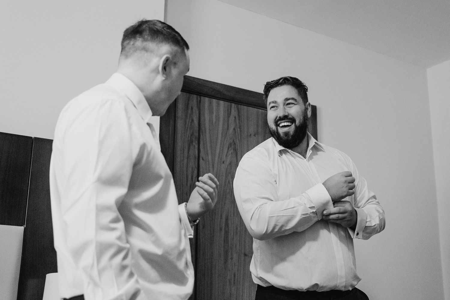 Two men in white button-up shirts share a candid moment of laughter in a black and white photograph. Wedding Photography Trim Castle Ireland