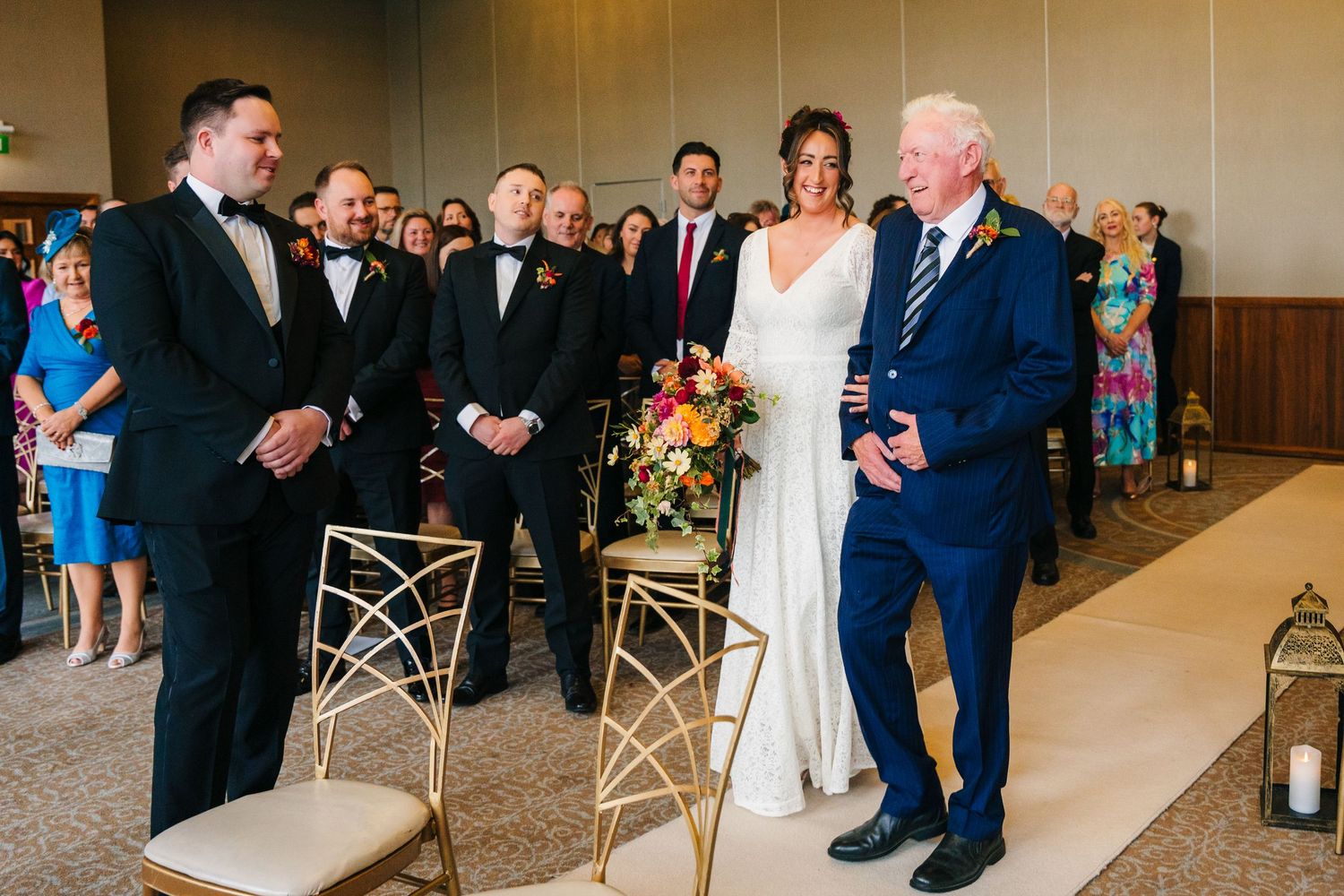 A wedding ceremony scene with guests gathered around decorative chairs and lanterns in an indoor venue. Wedding Photography Trim Castle Irel