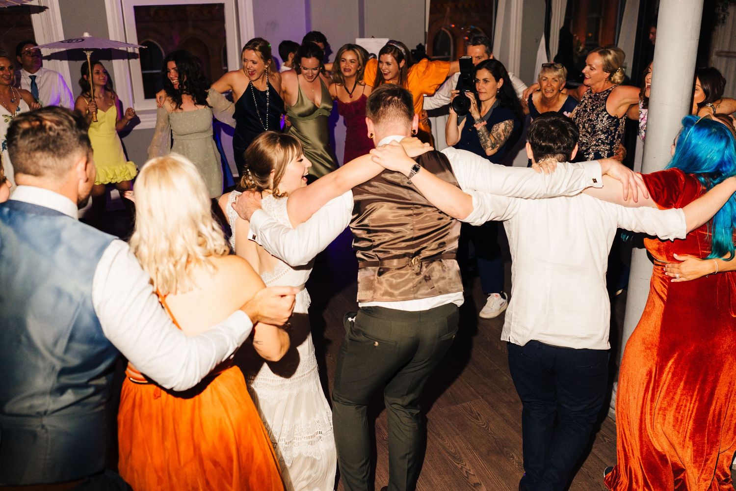 Energetic dance circle forms on the reception floor with guests in formal attire and colorful dresses. PHOTOGRAPHER Dublin Ireland Wedding