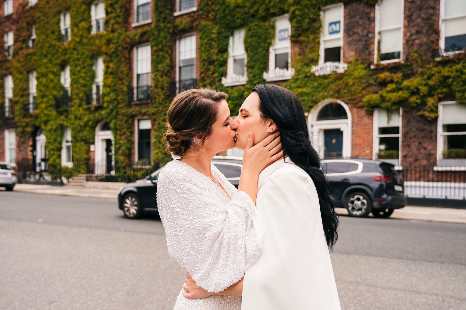 Two people in white outfits share an intimate moment on a street with ivy-covered buildings in the background. House Dublin Wedding Photogra
