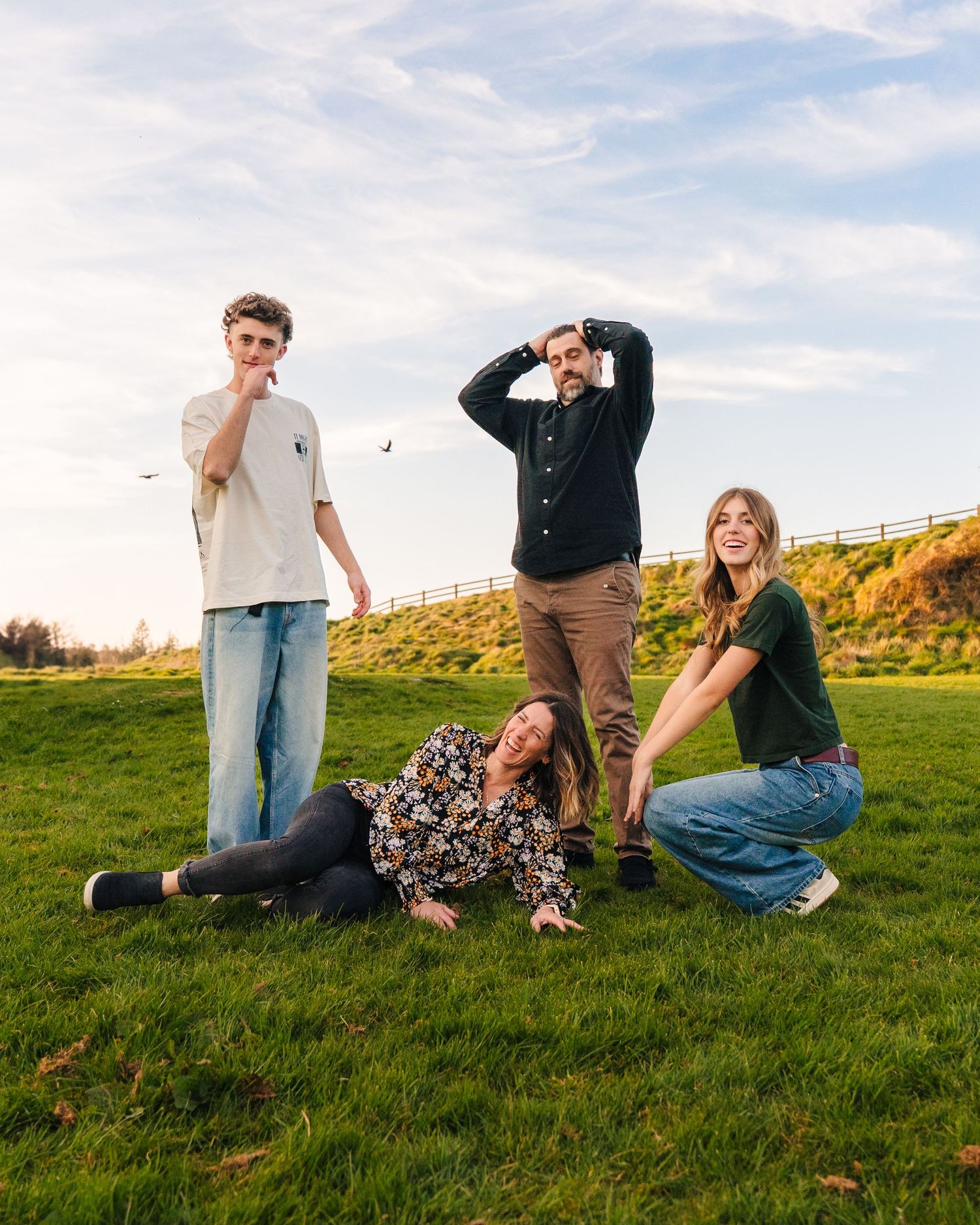 A group playfully tumbles and poses together on a grassy hillside during golden hour. Family photographer dublin