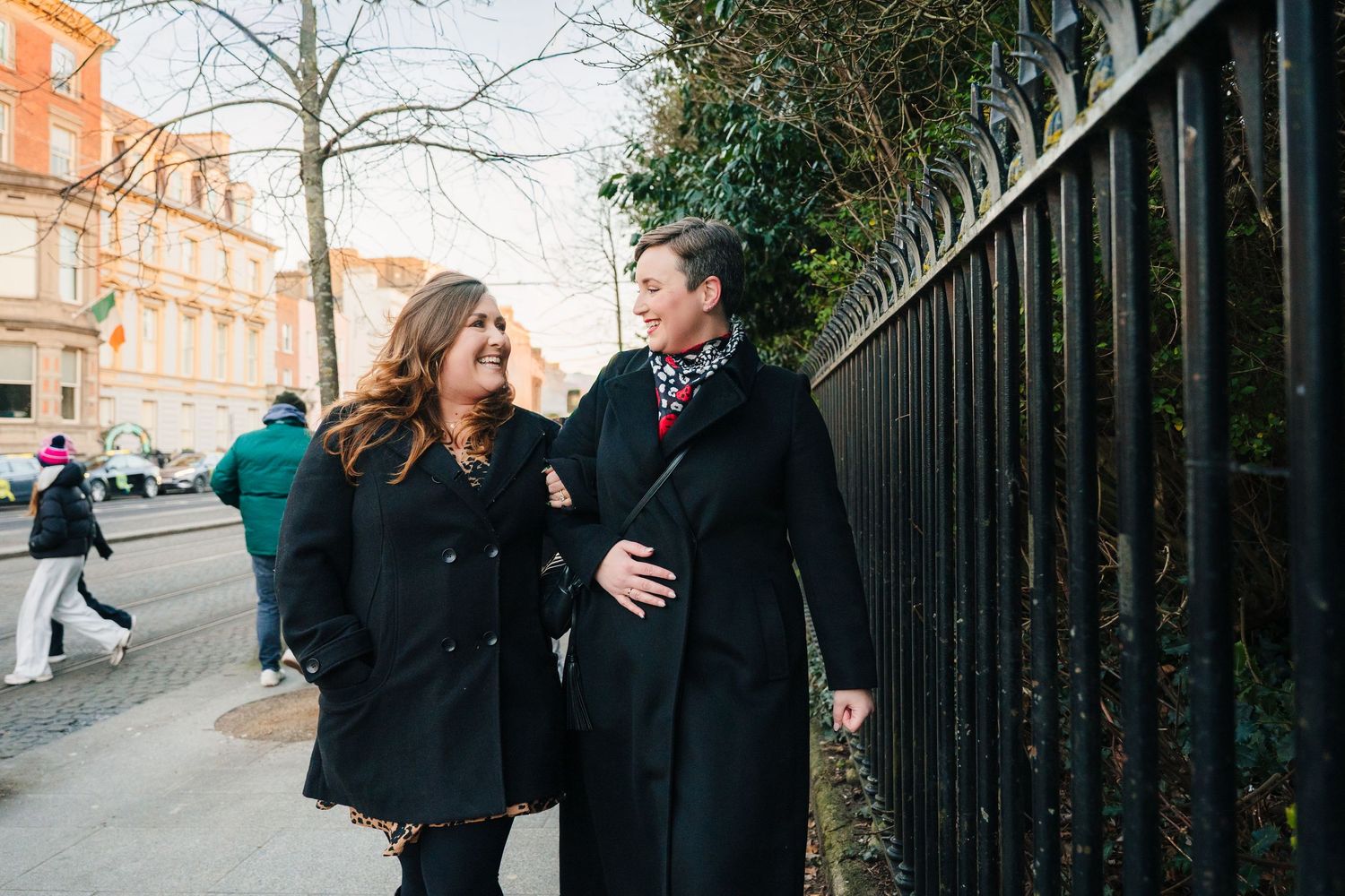 Couple walking together along an iron fence on a winter city street. family PHOTOGRAPHER Dublin
