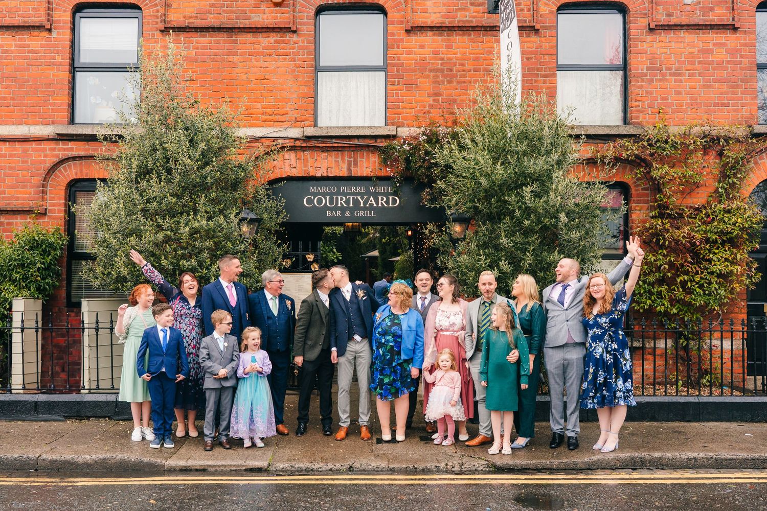 Group photo of wedding guests lined up against a red brick building exterior. Marco Pierre Dublin Wedding Photographer