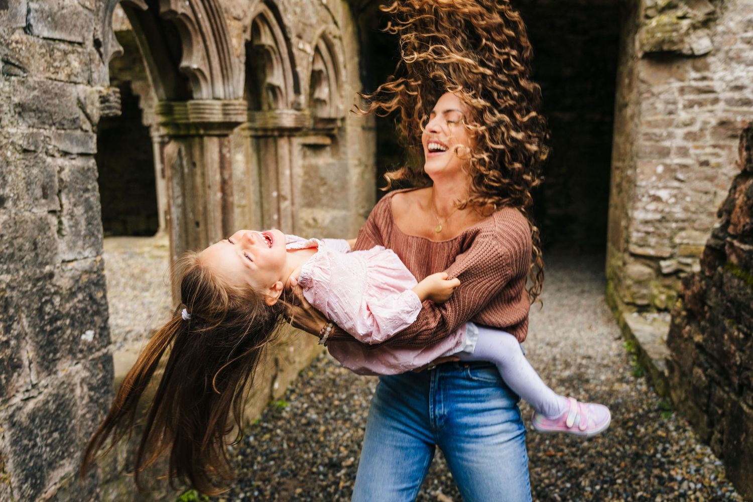 Two friends sharing a joyful moment together while playing in a stone archway of a historic building. family PHOTOGRAPHER Dublin