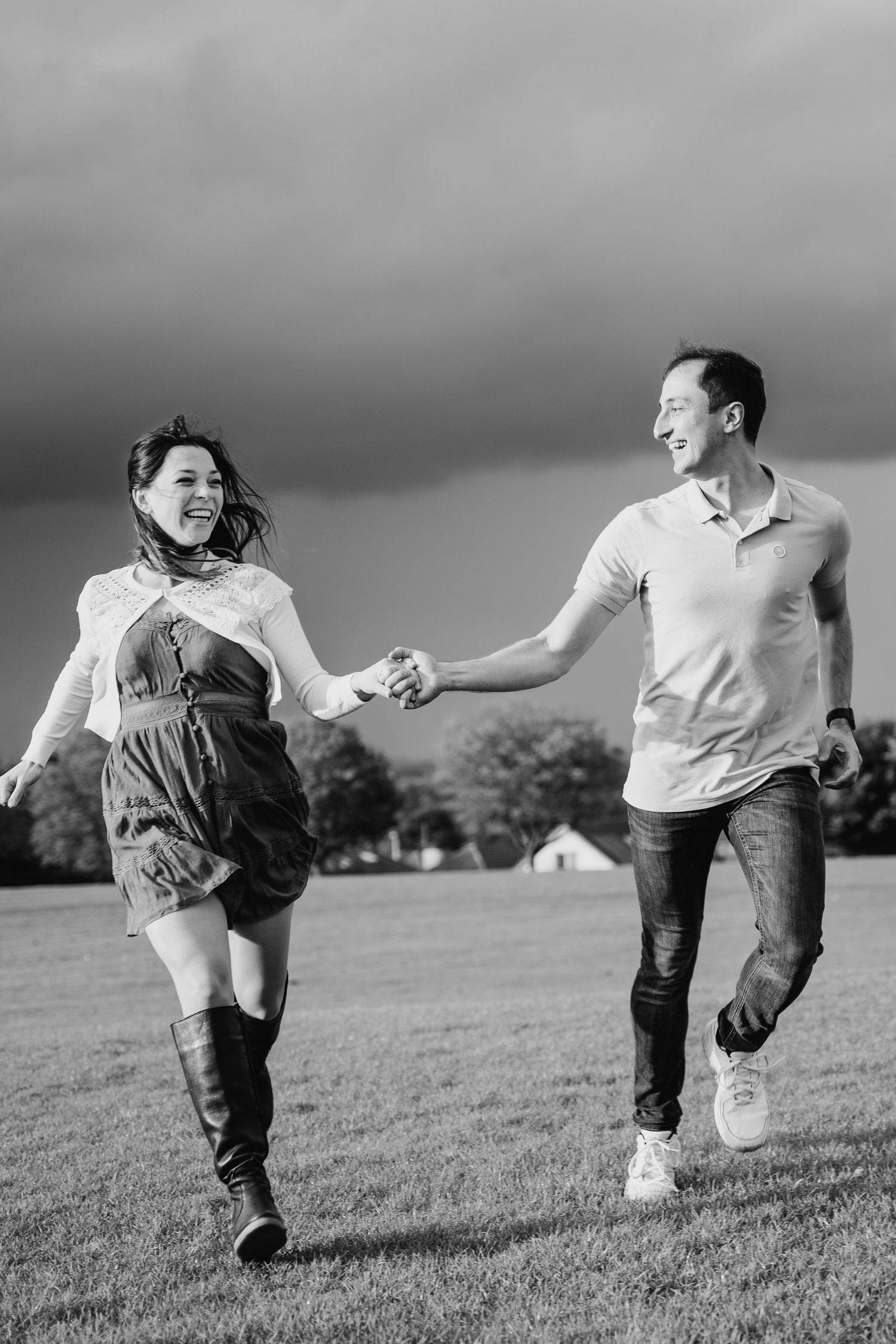 A joyful couple runs hand-in-hand through a grassy field under dramatic cloudy skies in black and white. PHOTOGRAPHER Dublin ireland