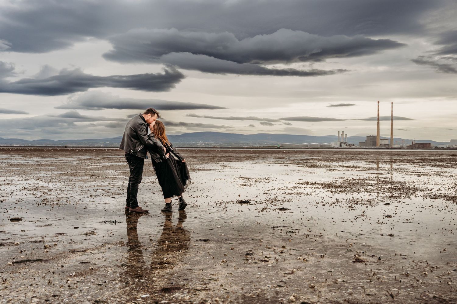 A couple embraces on a barren salt flat under dramatic storm clouds, with utility poles in the distance.PHOTOGRAPHER Dublin ireland