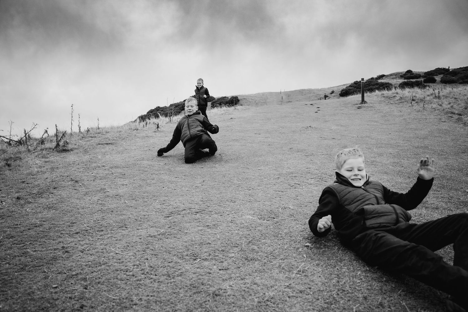 Two people slide down a sandy dune on a cloudy day in black and white photography. family PHOTOGRAPHER Dublin