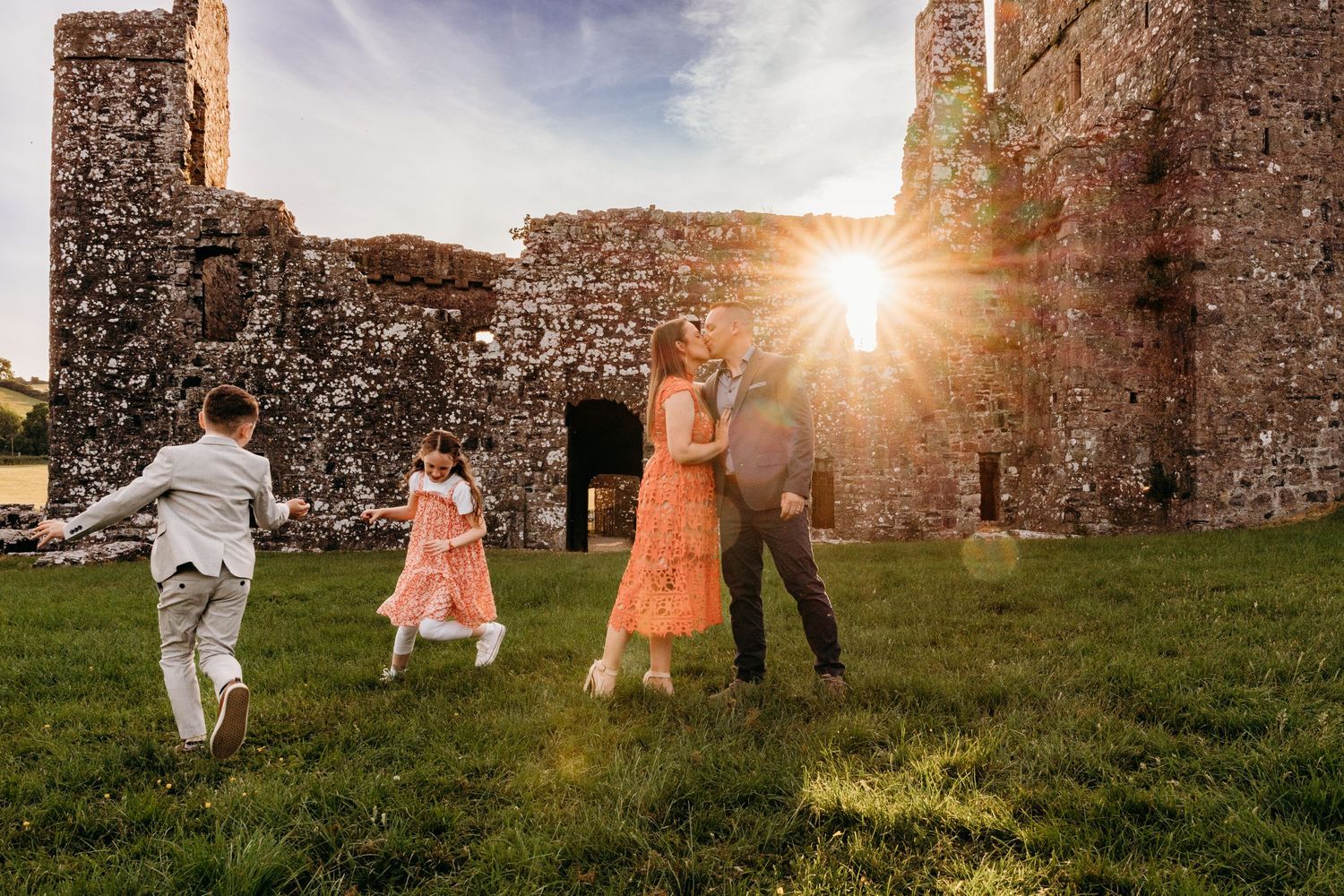 A family holds hands while running through the grass at sunset near ancient stone castle ruins. family PHOTOGRAPHER Dublin